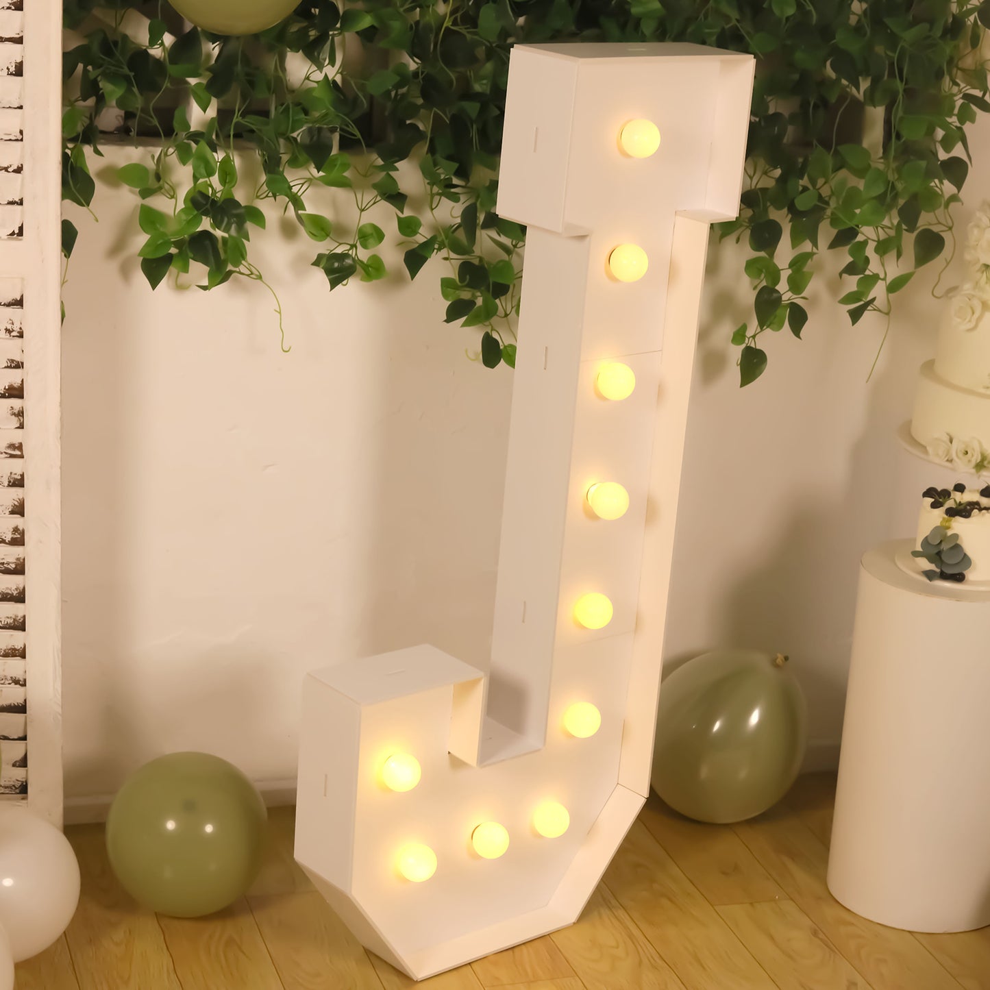 White LED marquee letter "J" with warm white lights, surrounded by greenery.