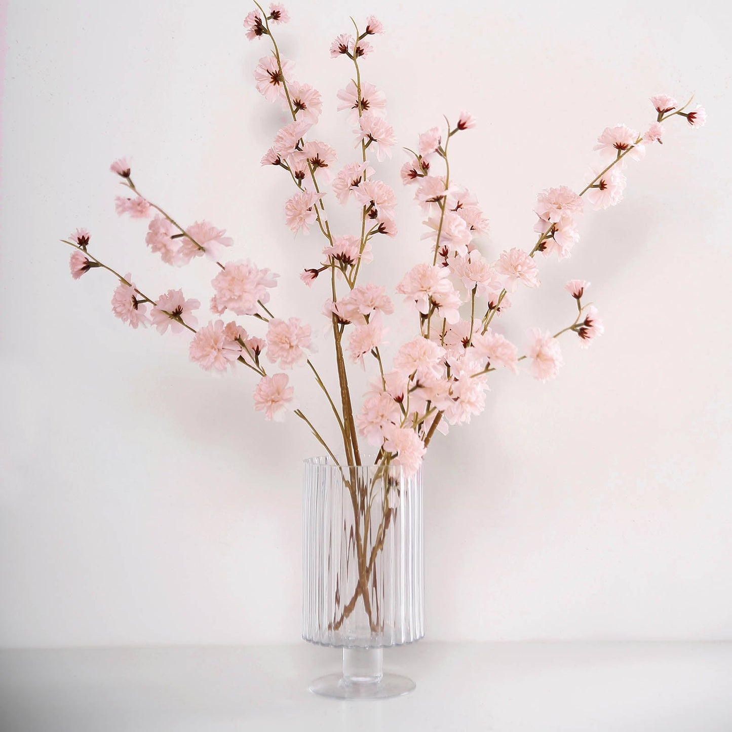 Blush artificial silk carnation flower stems in a clear vase.