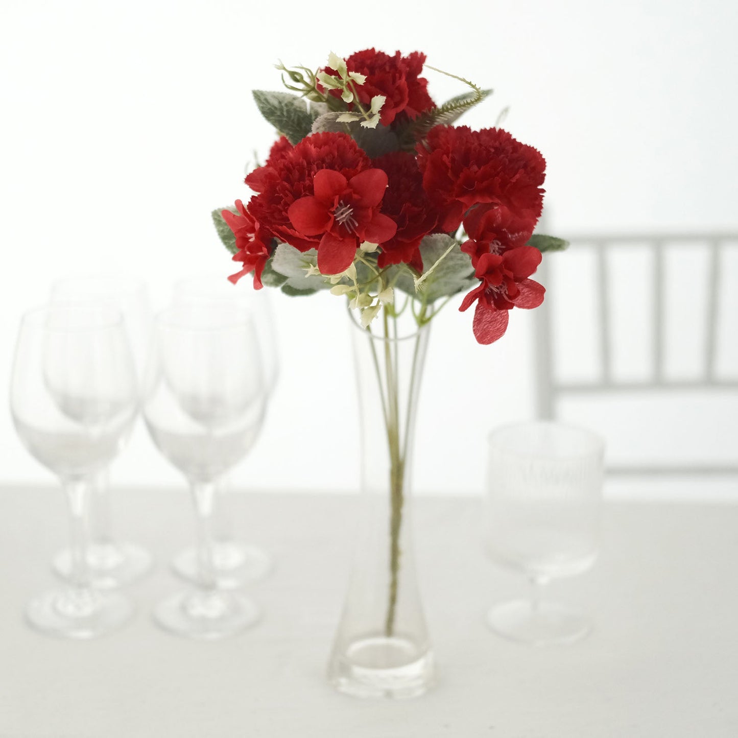 Red artificial silk carnation flower bouquet in a clear vase.