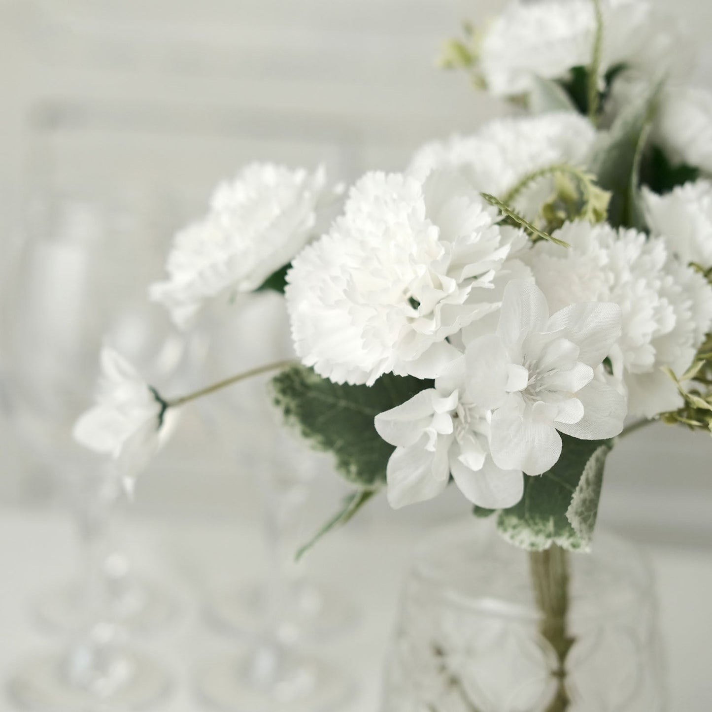 White artificial silk carnation flower bouquets in a glass vase.
