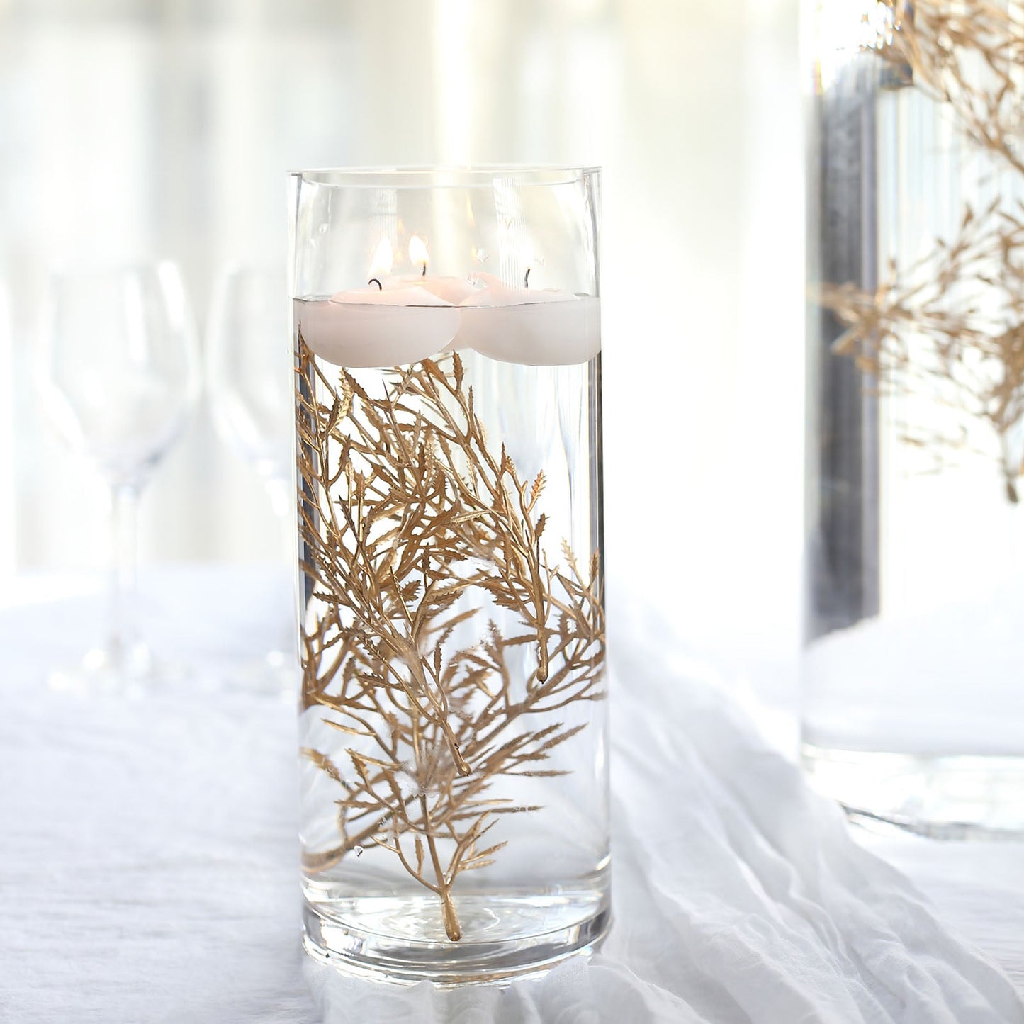 6" metallic gold artificial fern leaf branch in a clear vase with floating candles.