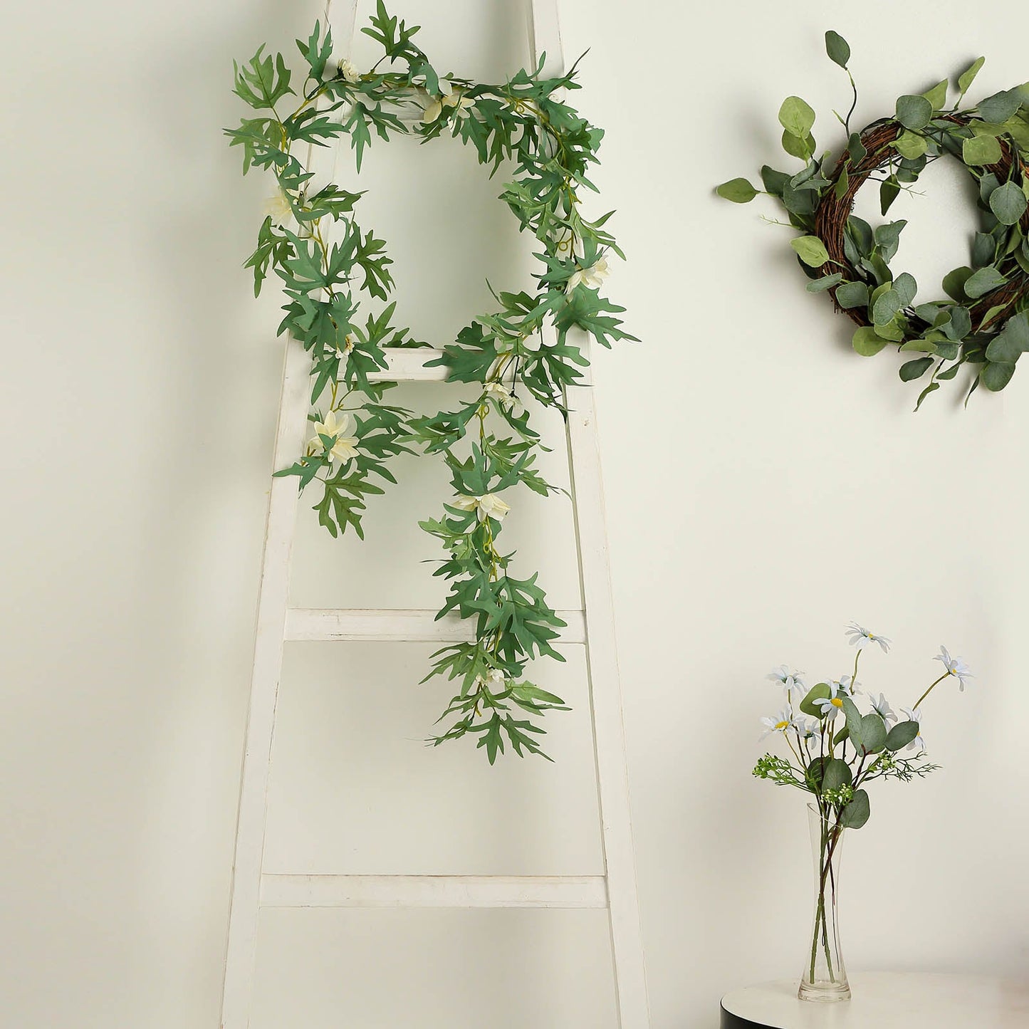 Cream artificial daisy and magnolia leaf garland on a ladder.