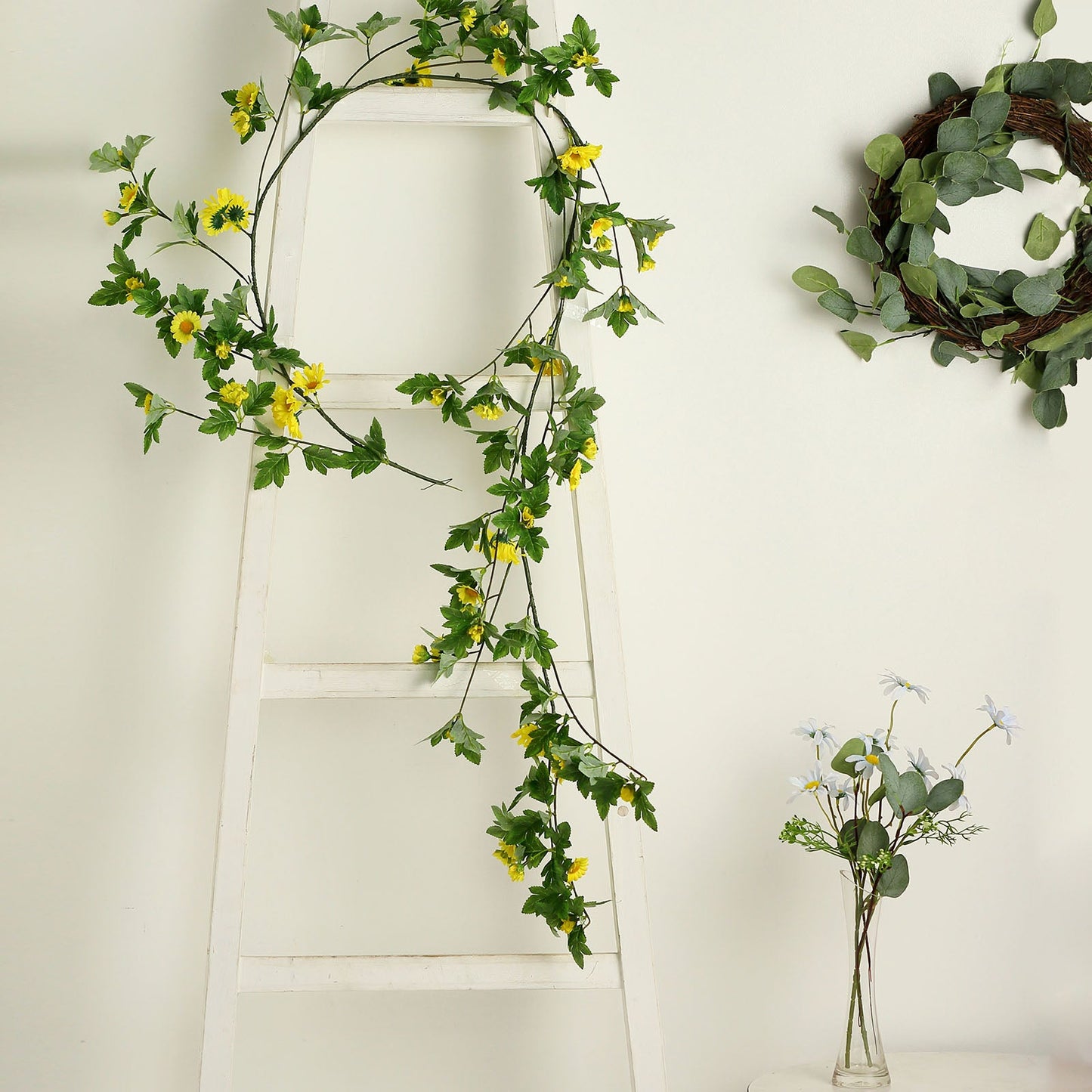 Yellow artificial daisy garland with green leaves on a white ladder.