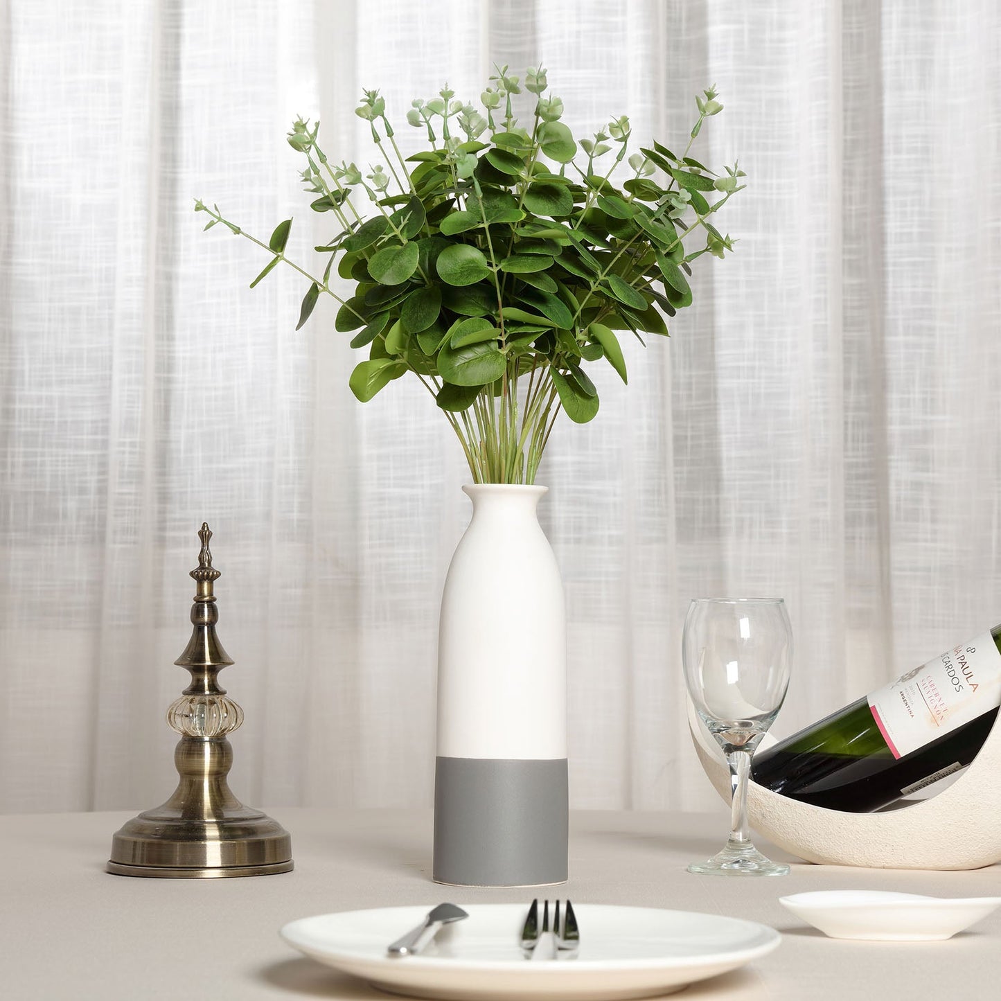 Light green artificial eucalyptus branch bouquet in a white vase.