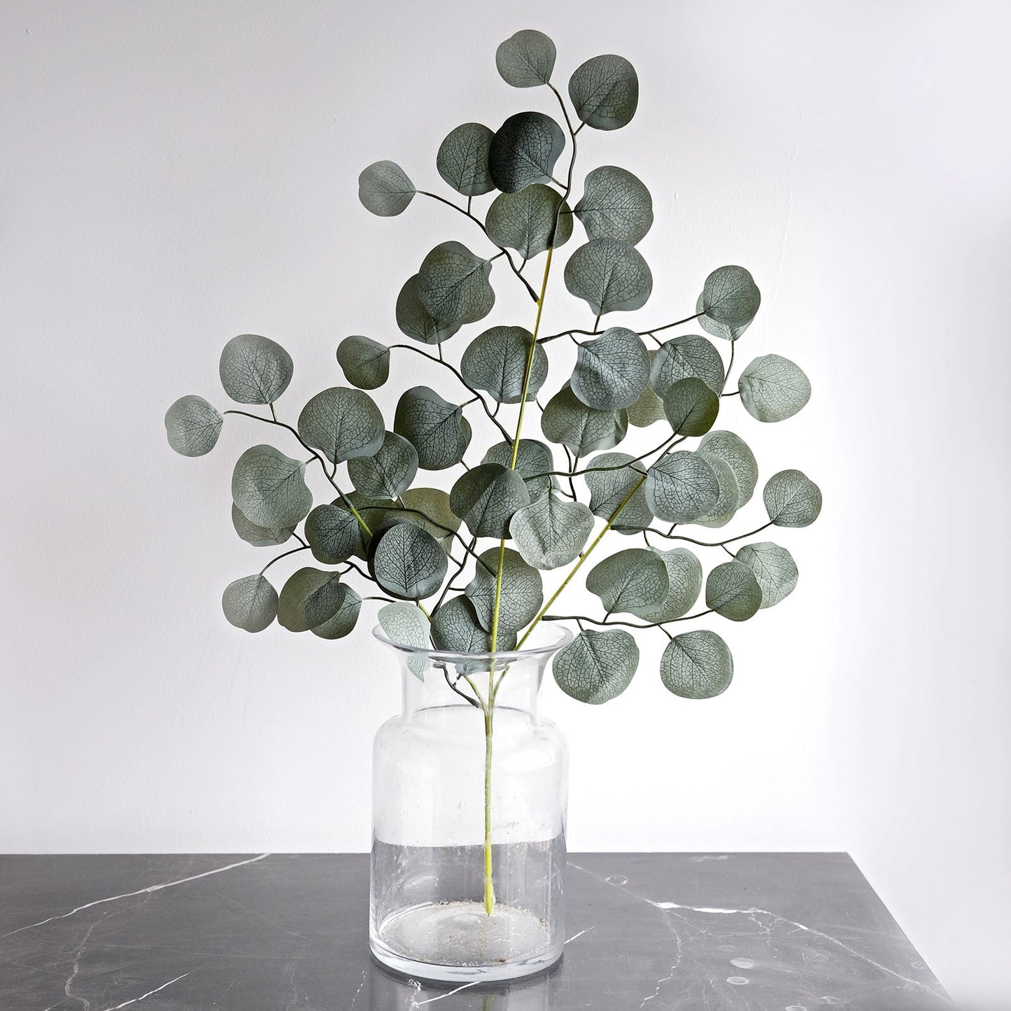 Frosted green artificial silk eucalyptus leaf stems in a glass vase.
