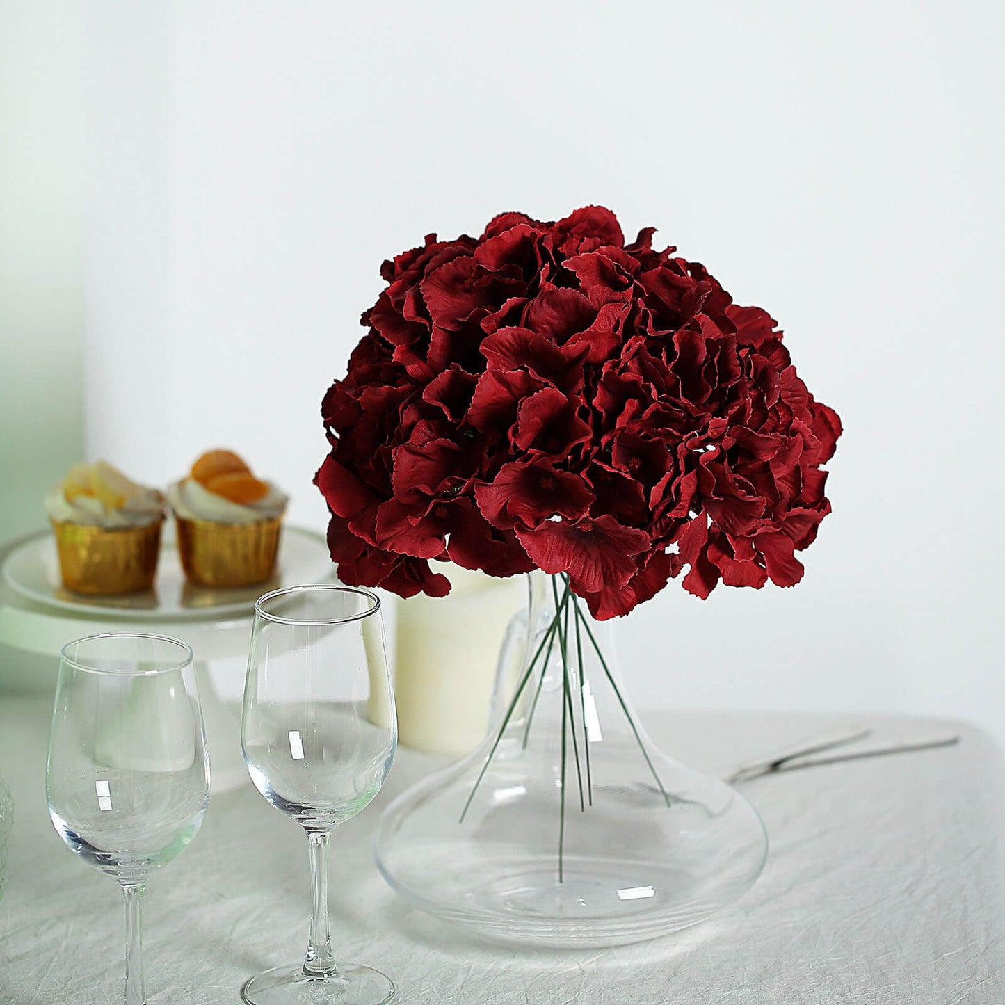 Burgundy artificial satin hydrangeas in a glass vase.