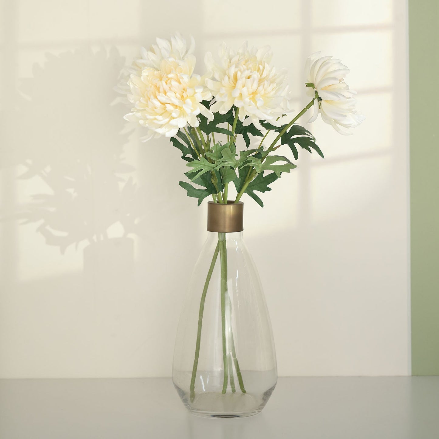 Ivory artificial silk chrysanthemum bouquet in a glass vase.