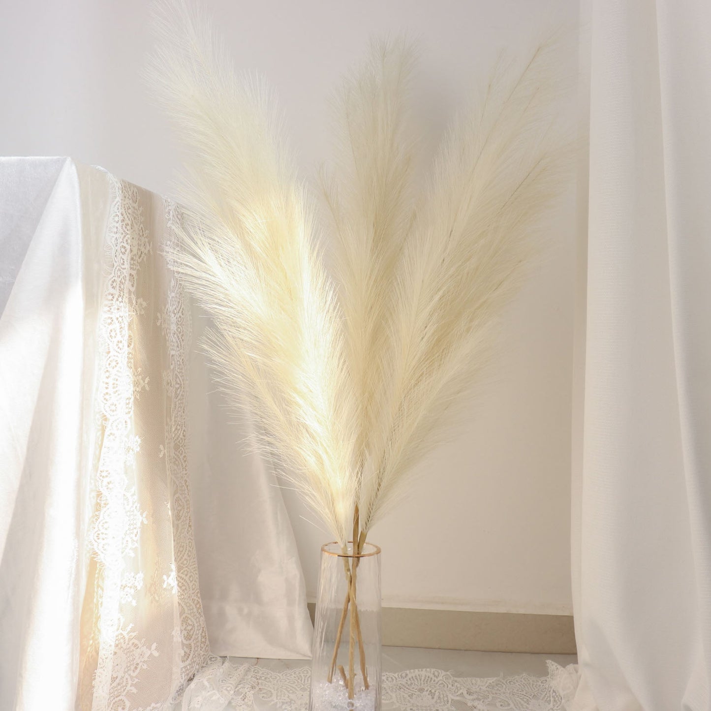 Cream artificial pampas grass plant sprays in a clear vase.