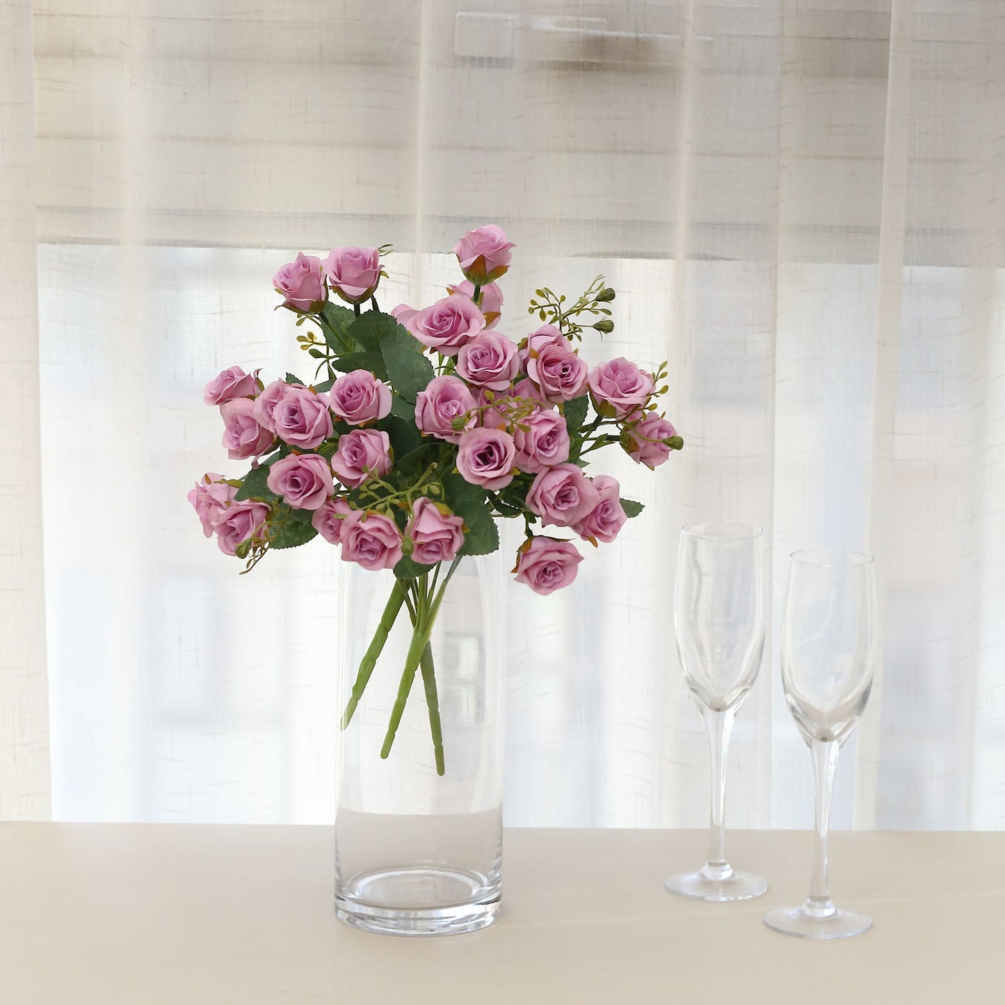 Lavender lilac artificial rose bouquet in a clear vase.