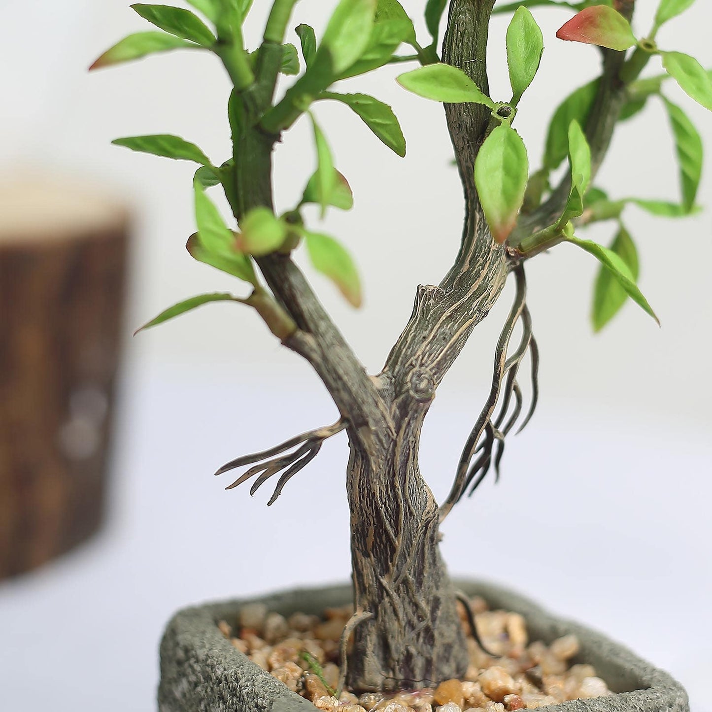 Concrete planter pot with artificial willow tree and green succulent leaves.