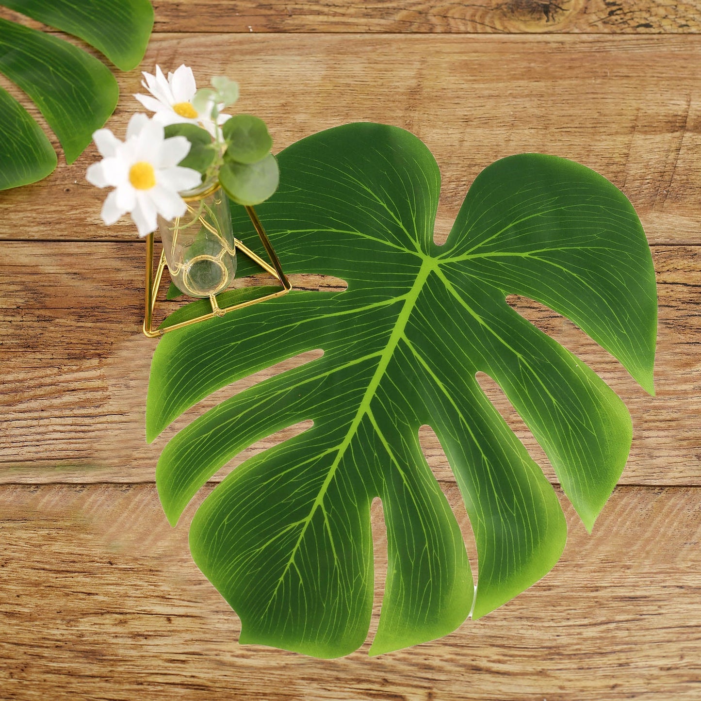 Green artificial tropical Monstera palm leaves on a wooden surface.