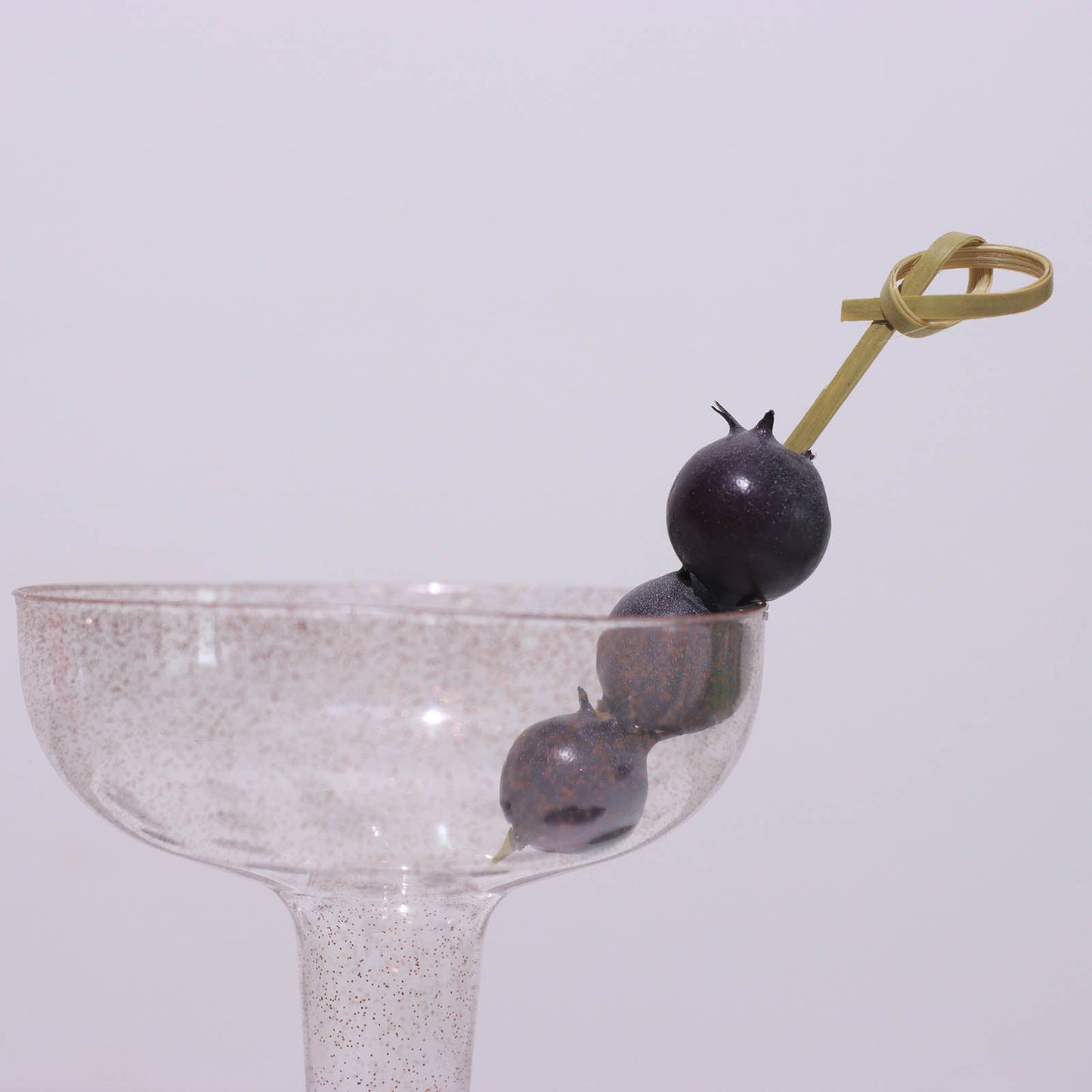 Eco-friendly knotted bamboo skewers in a glass with black olives.