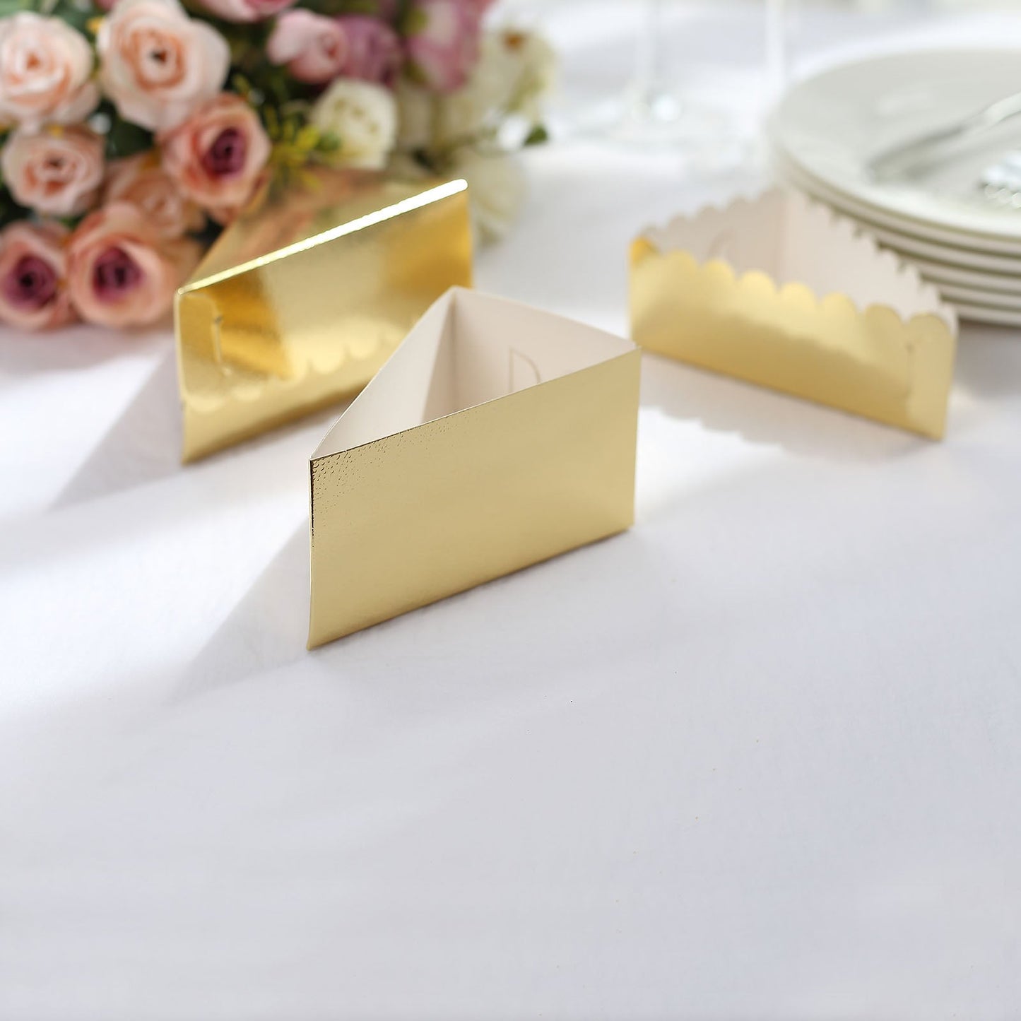Gold triangular cake boxes with scalloped tops on a table.