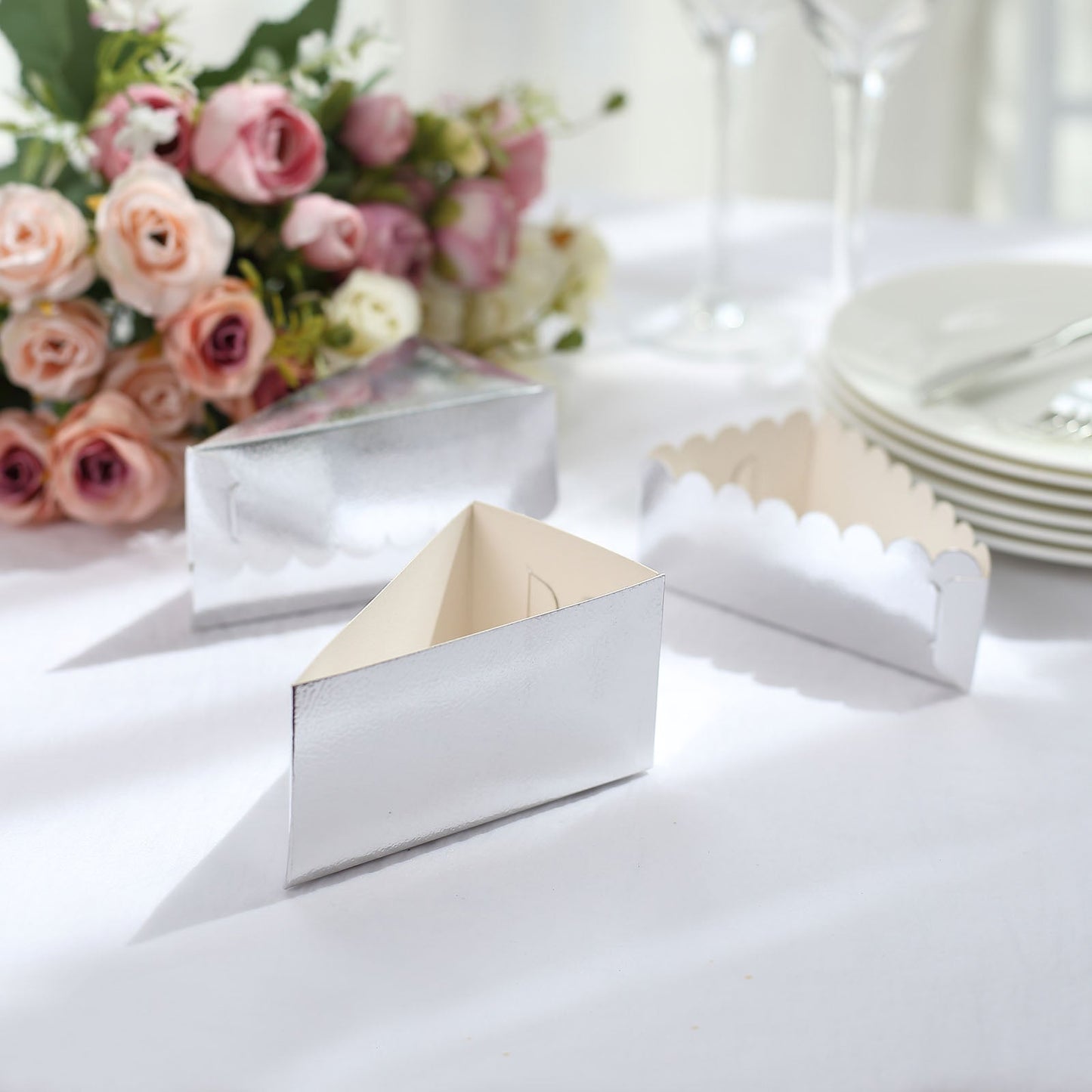 Silver triangular cake boxes with scalloped tops on a table setting.