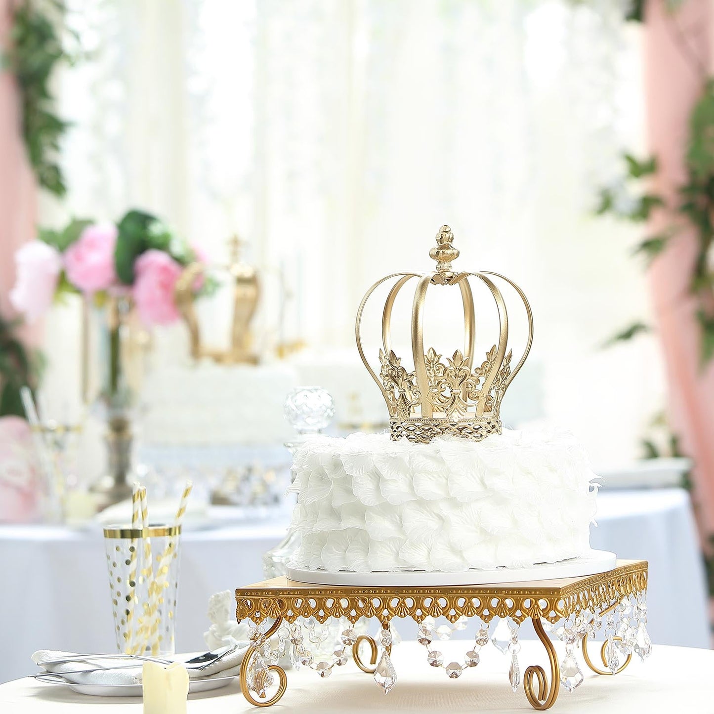 Gold metal fleur-de-lis crown cake topper on a white floral cake.