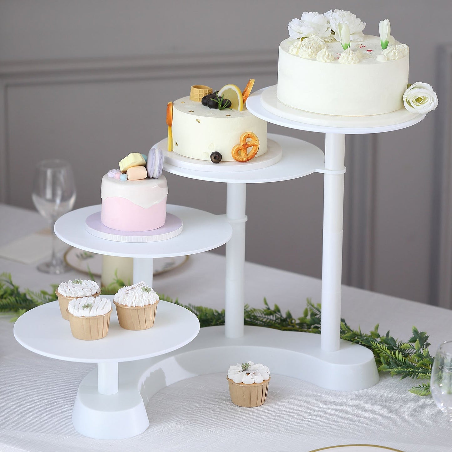 White 4-tier half moon plastic cake stand with cupcakes and desserts.