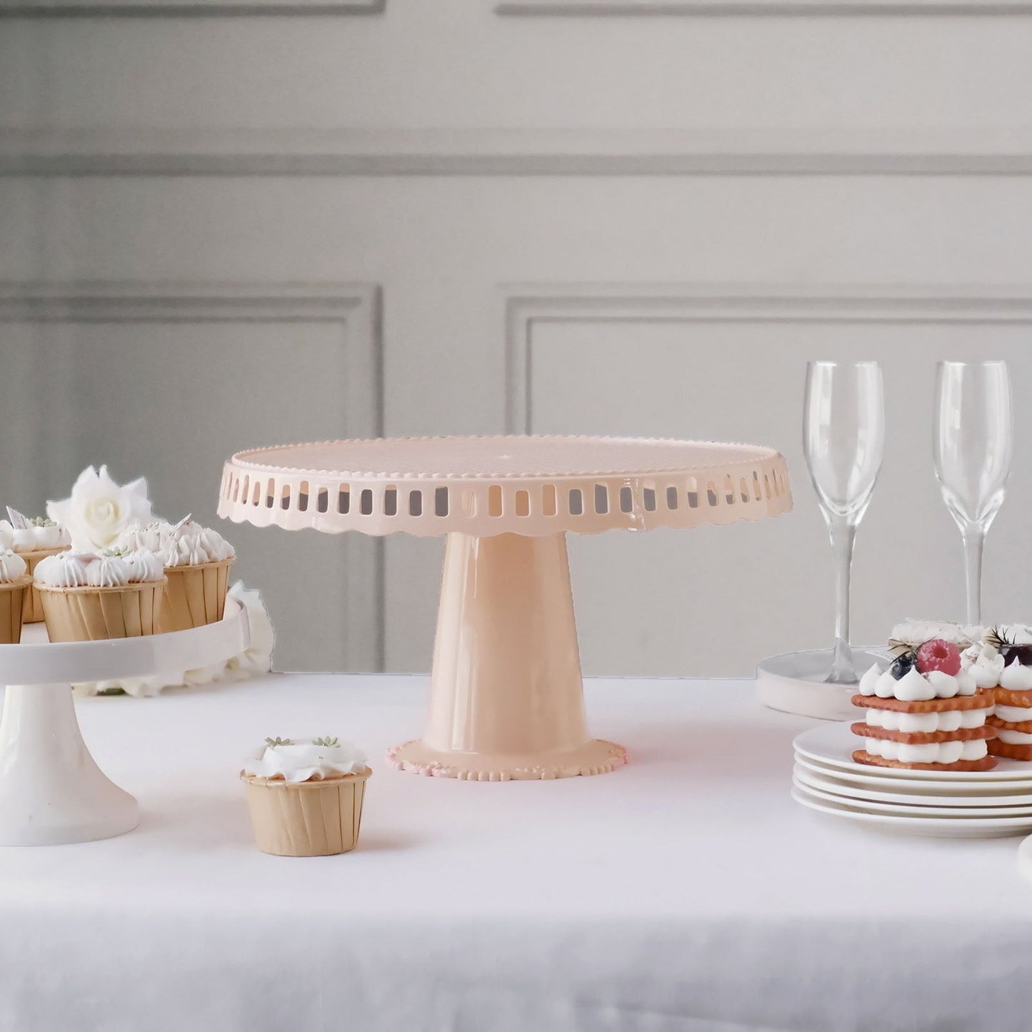 Blush round footed reusable plastic pedestal cake stand with scalloped edges.