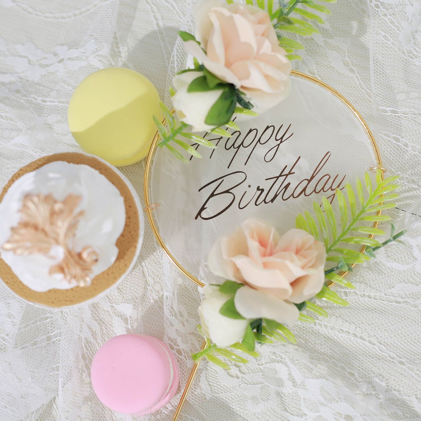 Gold acrylic Happy Birthday cake topper with silk flower clusters on a lace background.