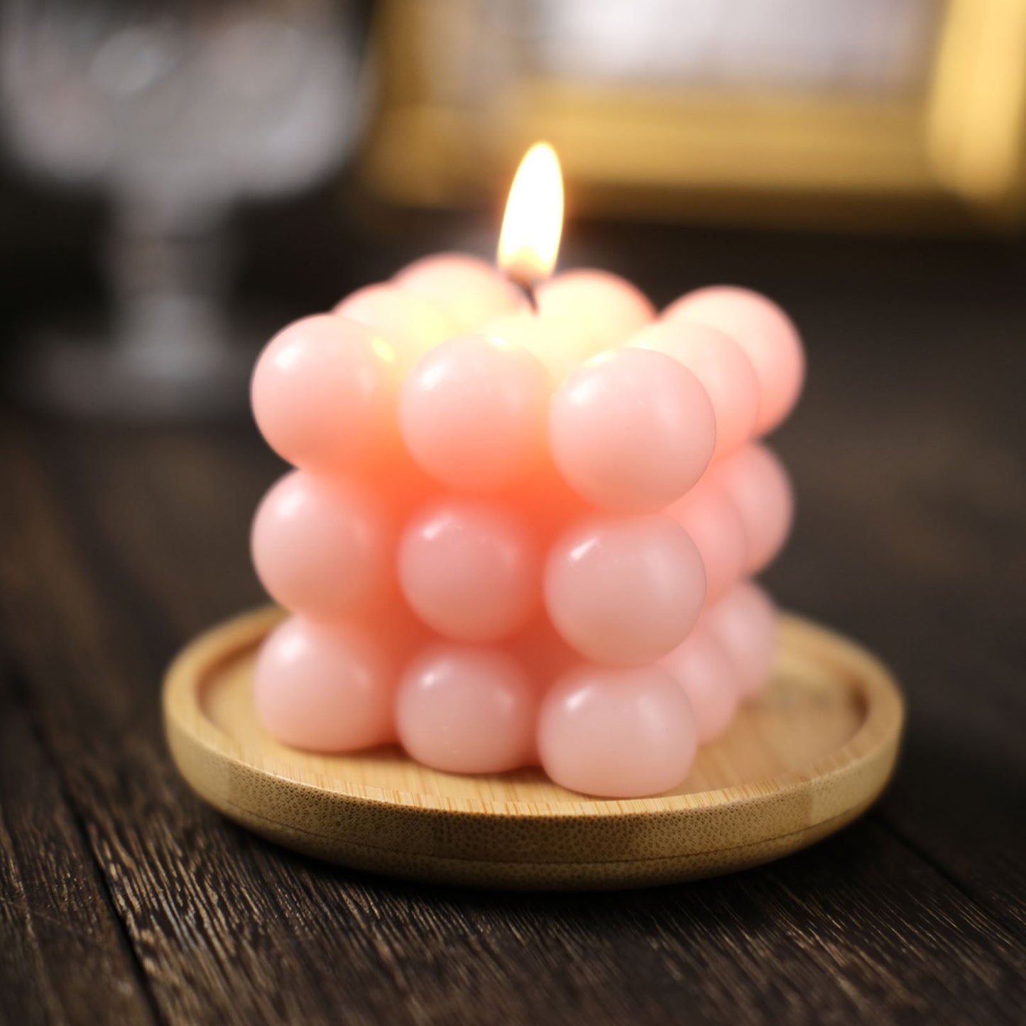 Pink blush bubble cube decorative candle on a wooden plate with a lit flame.