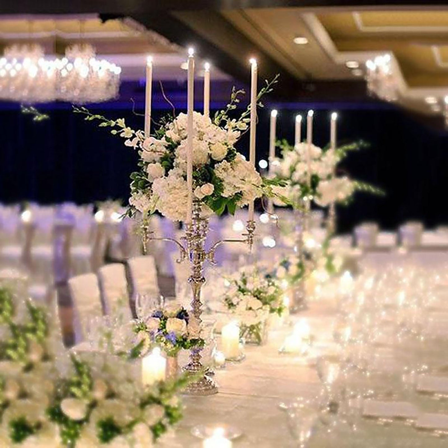 Silver metal 4 arm candelabra with floral arrangements and candles.