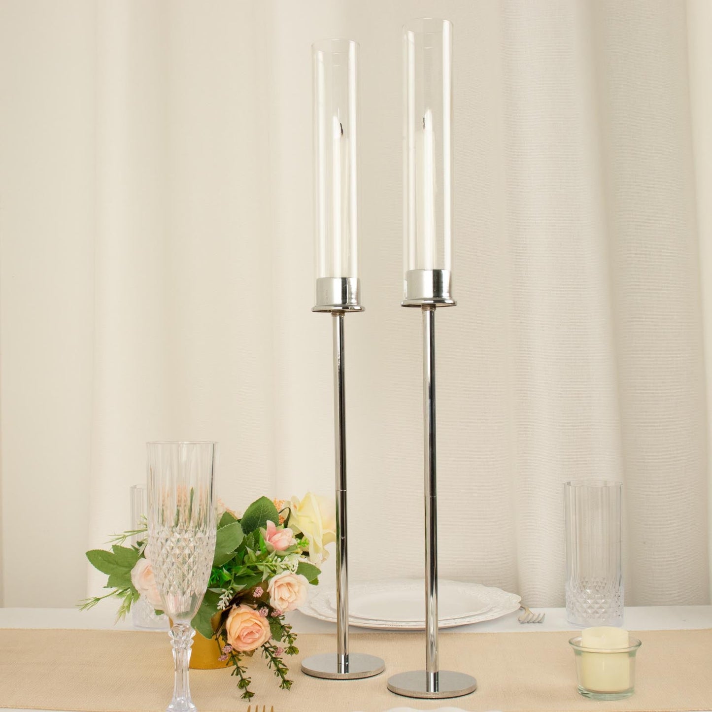 Silver metal candlestick holders with clear glass chimneys for taper candles.