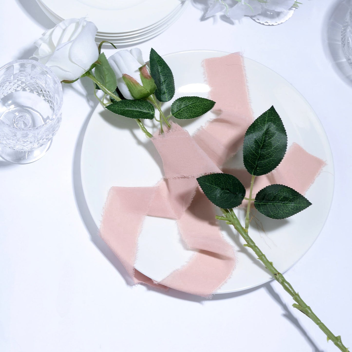 Blush chiffon linen ribbon roll on a white plate with roses and leaves.