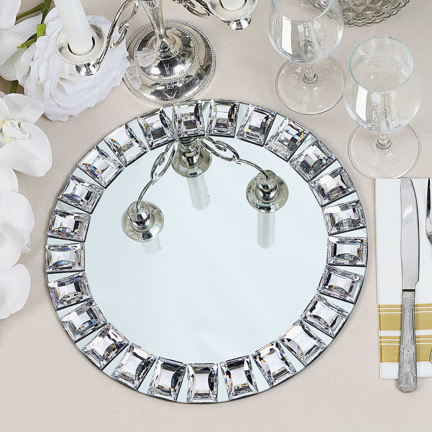 Silver jeweled rim glass mirror charger plate on a table setting.