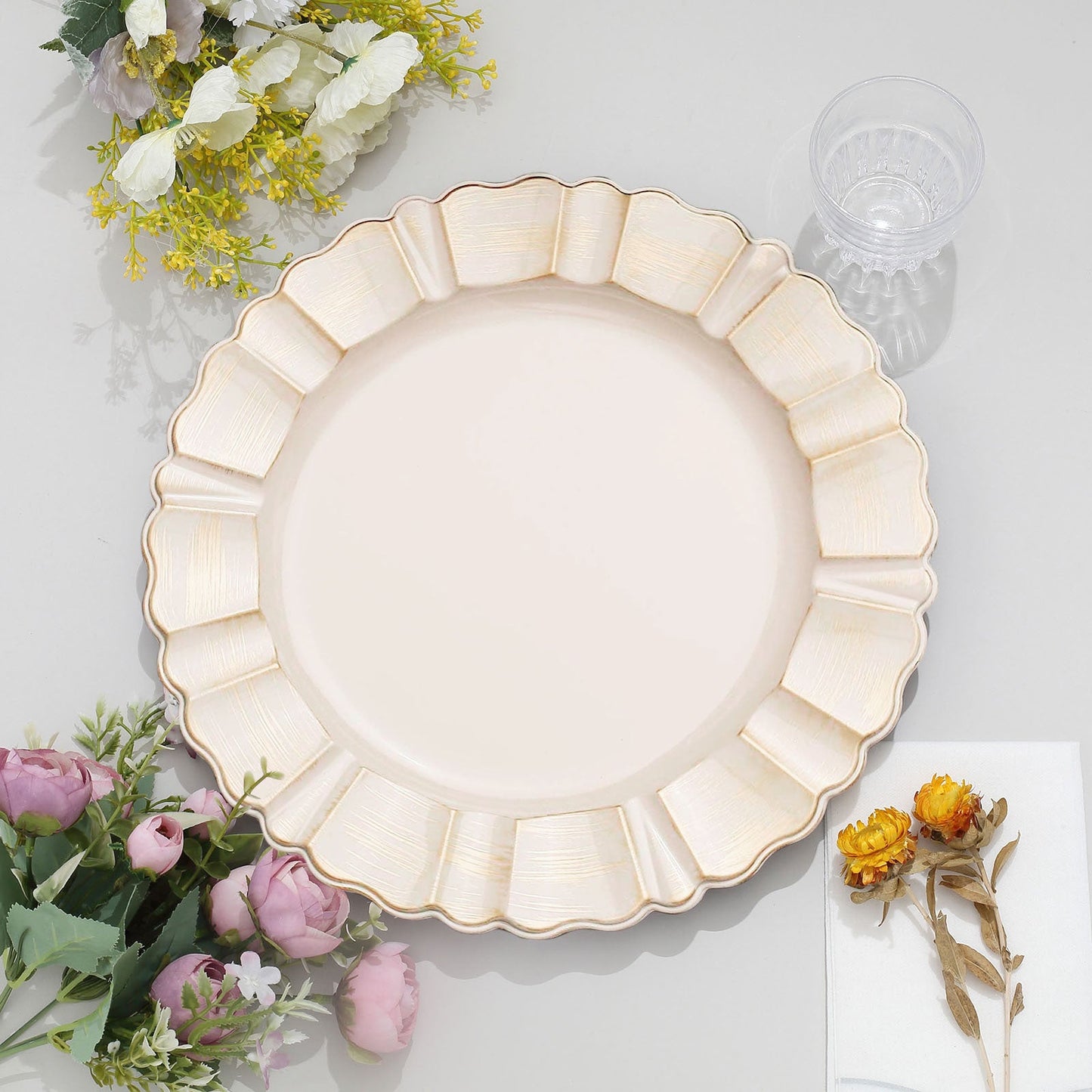 Beige acrylic dinner plate charger with gold scalloped rim on a table setting.