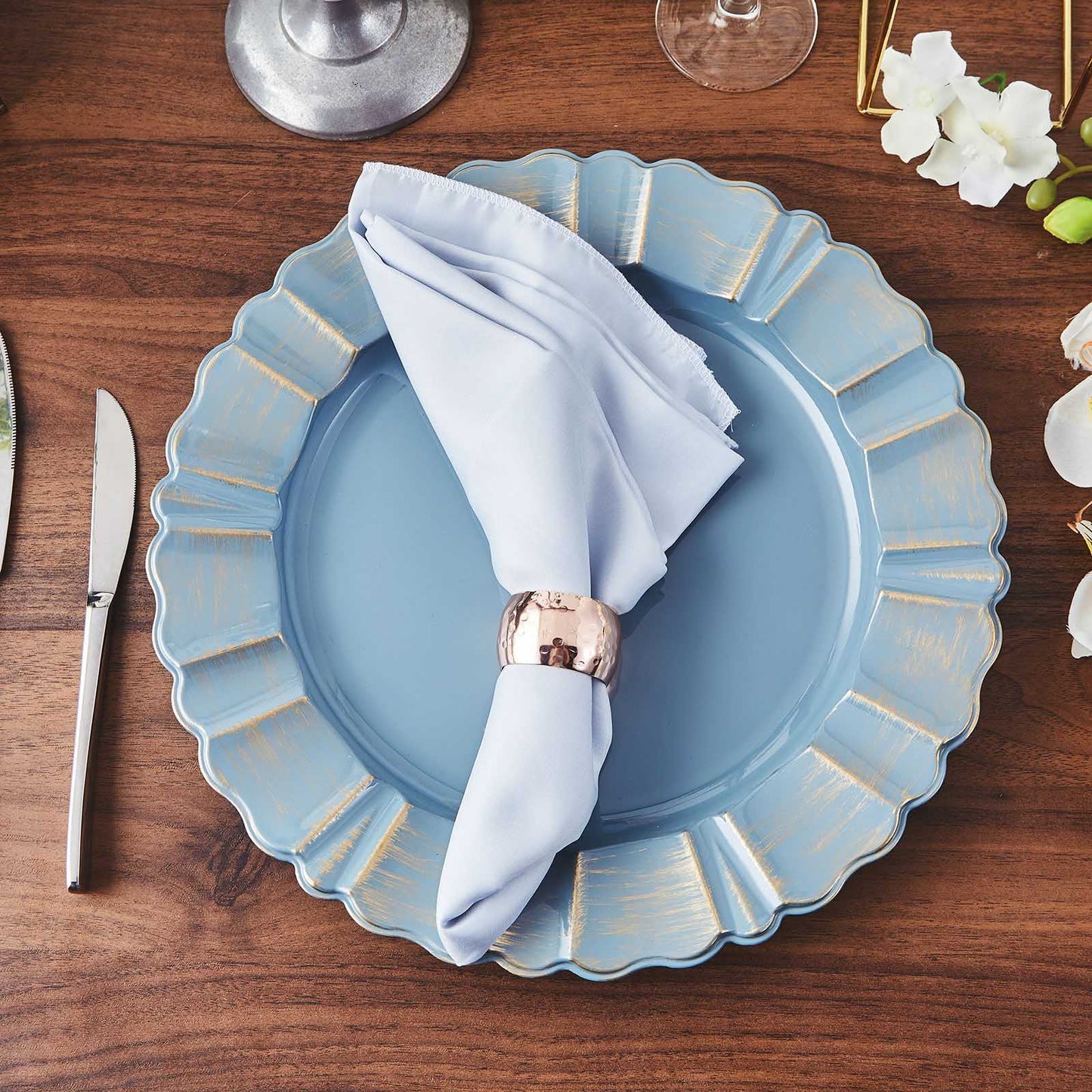Dusty blue charger plate with gold brushed scalloped rim on a wooden table.