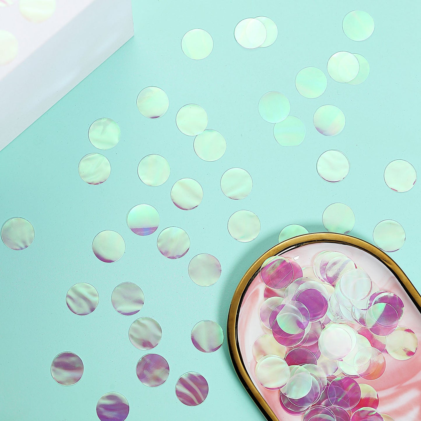 Iridescent round foil metallic confetti dots on a mint green surface.