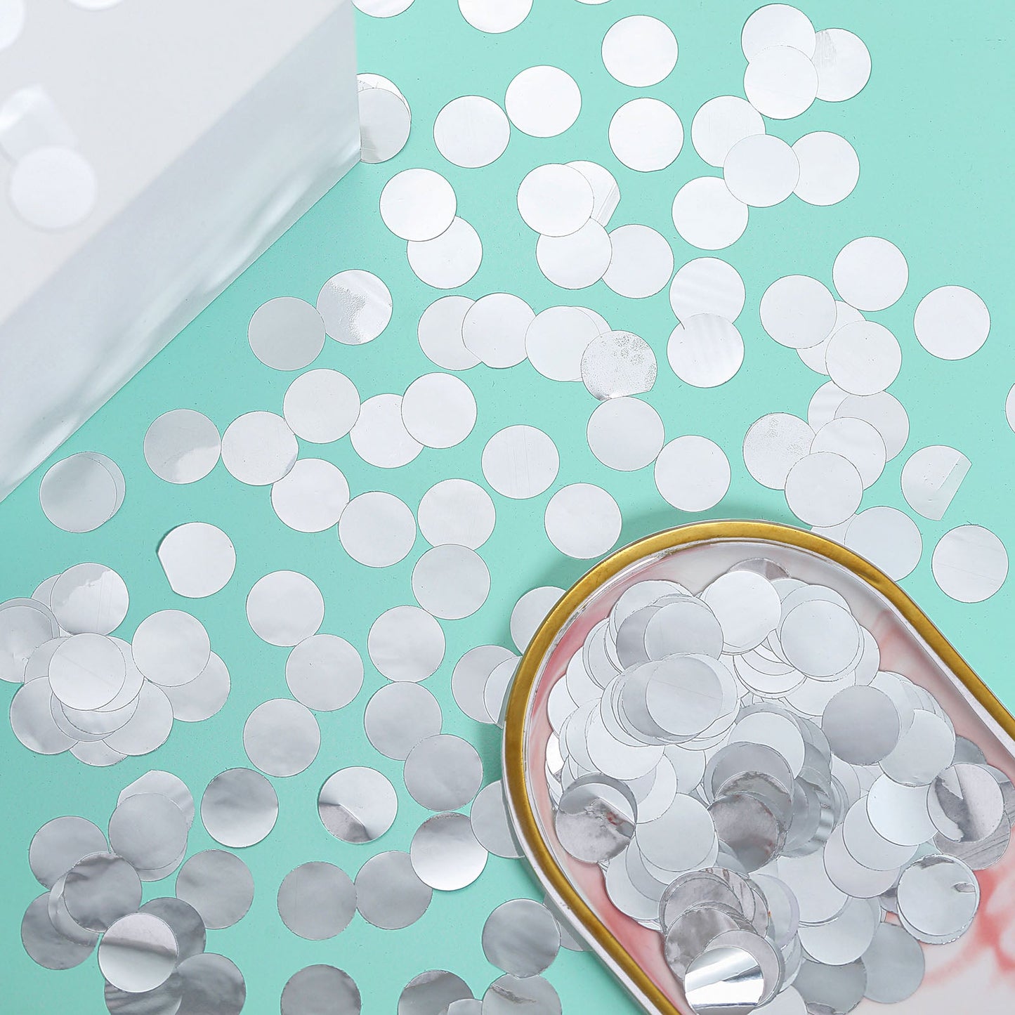 Silver round foil metallic table confetti dots on a mint green surface.