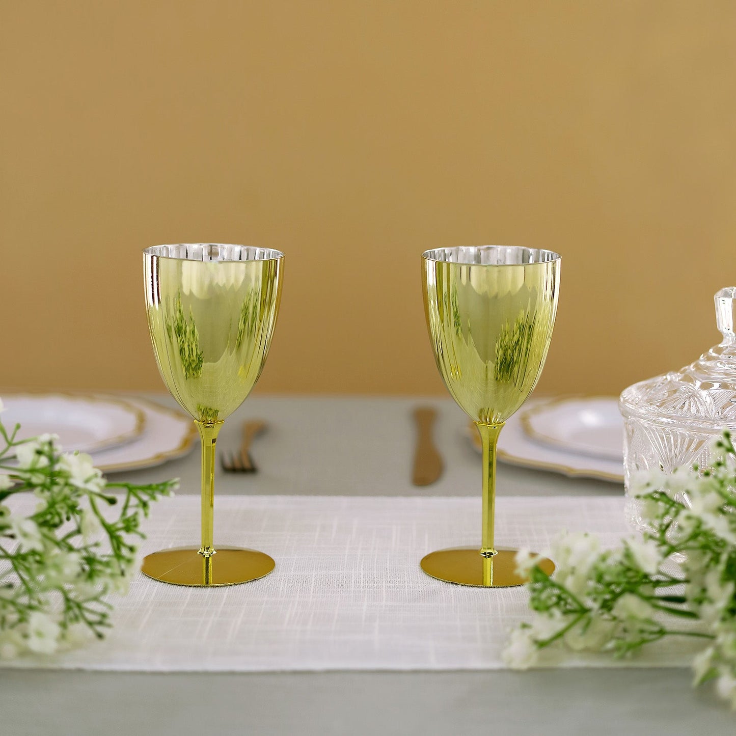 Gold disposable wine glasses on a table with flowers.