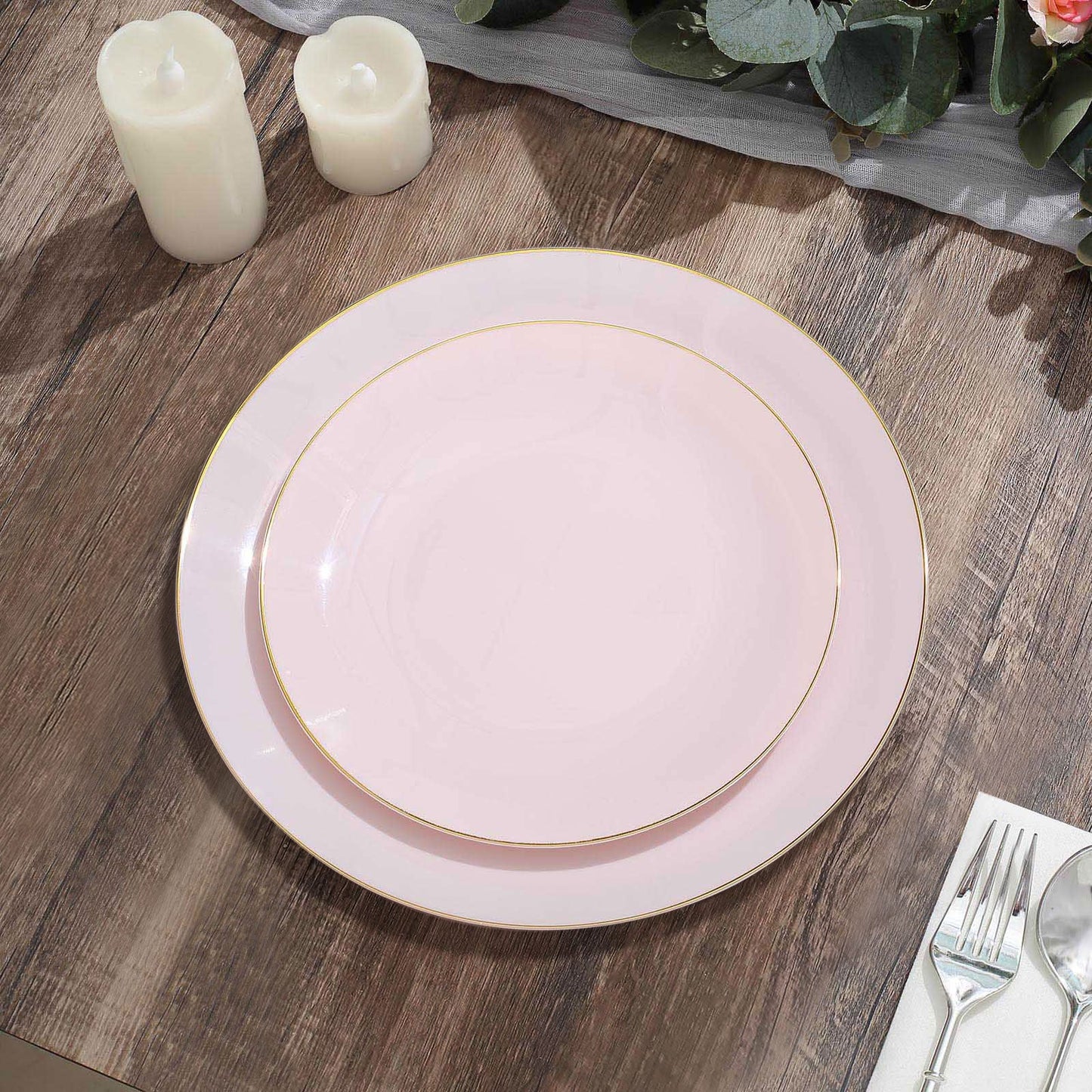 Glossy blush round plastic dessert plates with gold rim on a wooden table.
