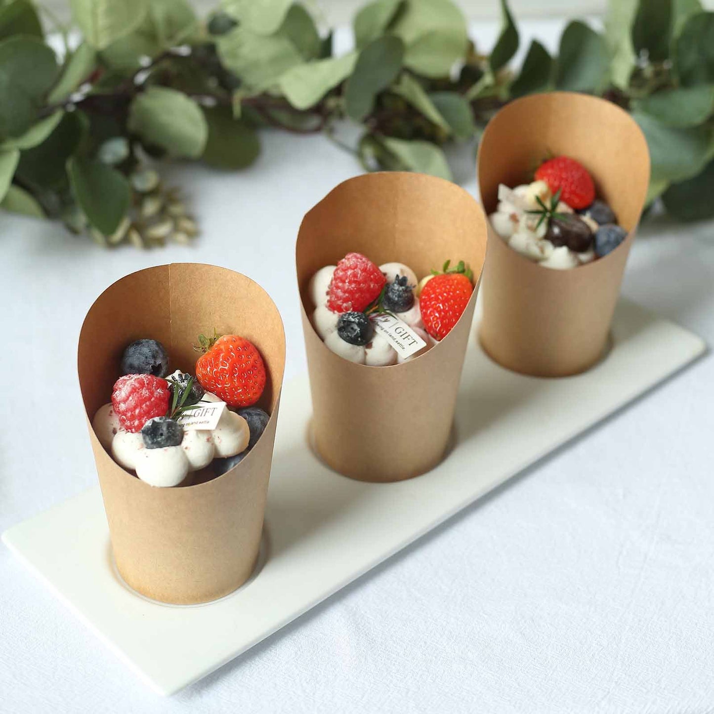 Natural brown paper popcorn cups with assorted berries and whipped cream.