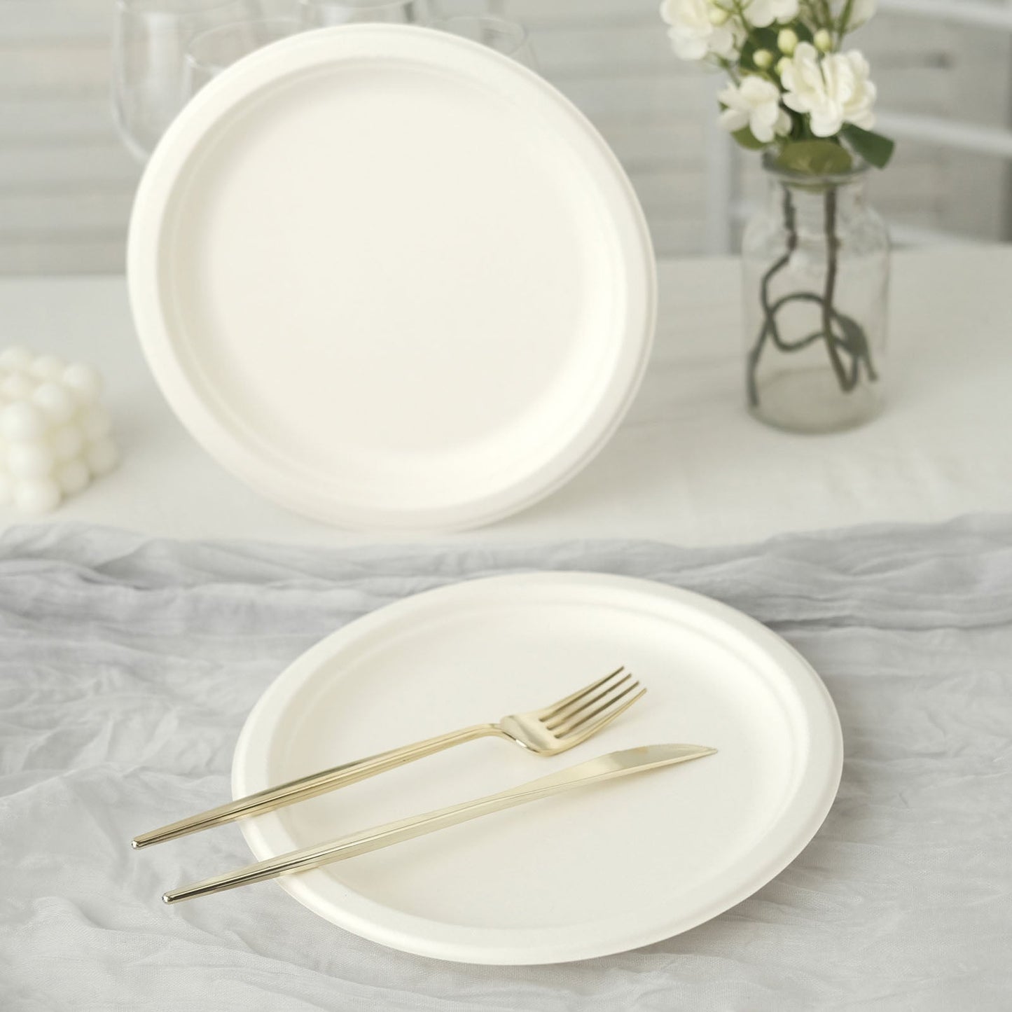 White biodegradable bagasse dinner plates on a table with gold utensils.