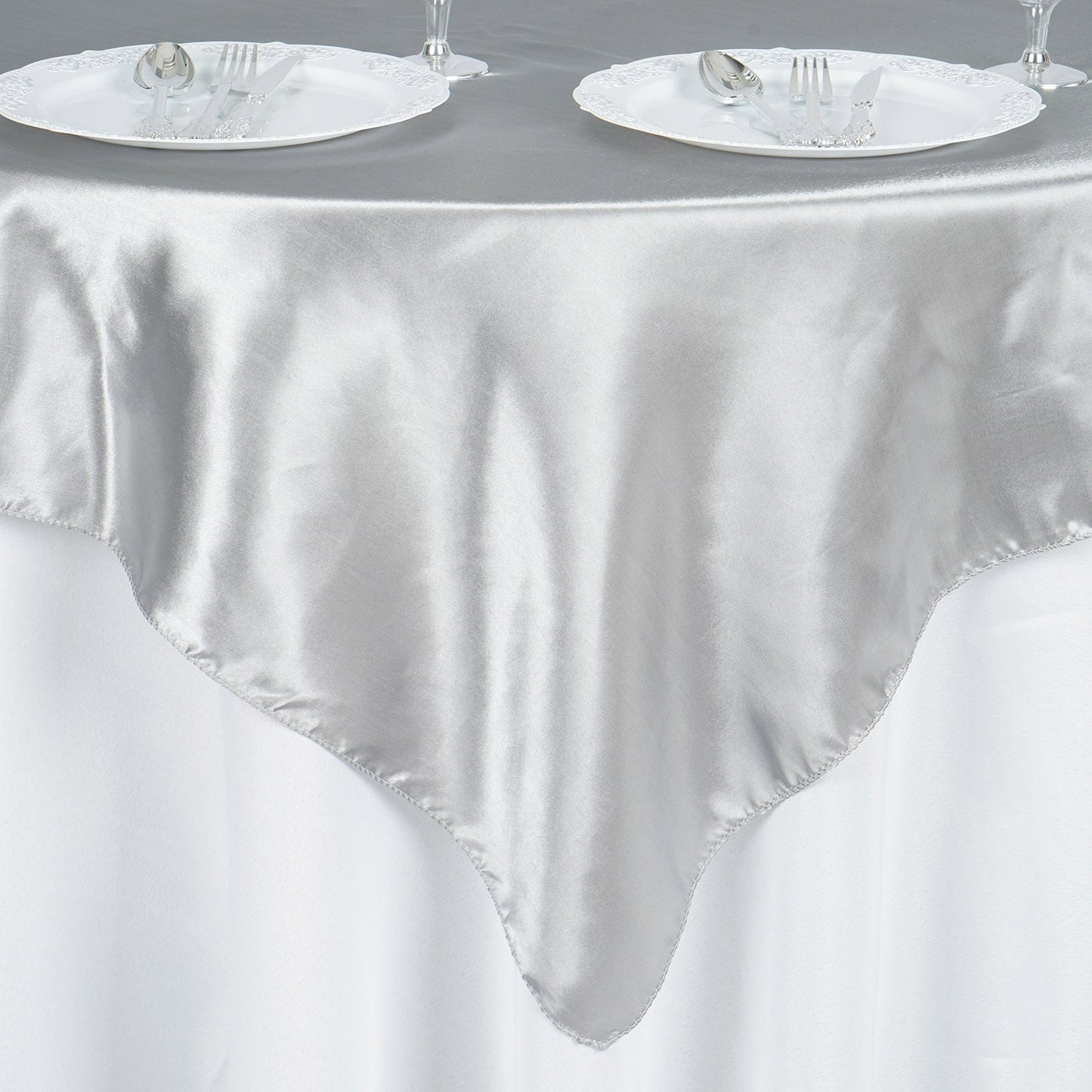 Silver satin table overlay on a round table with plates and cutlery.