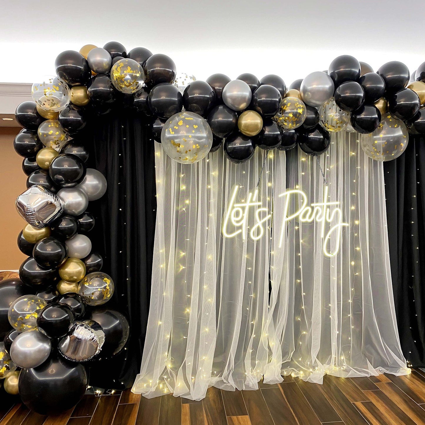 Neon "Let's Party" sign with black and gold balloon decor.