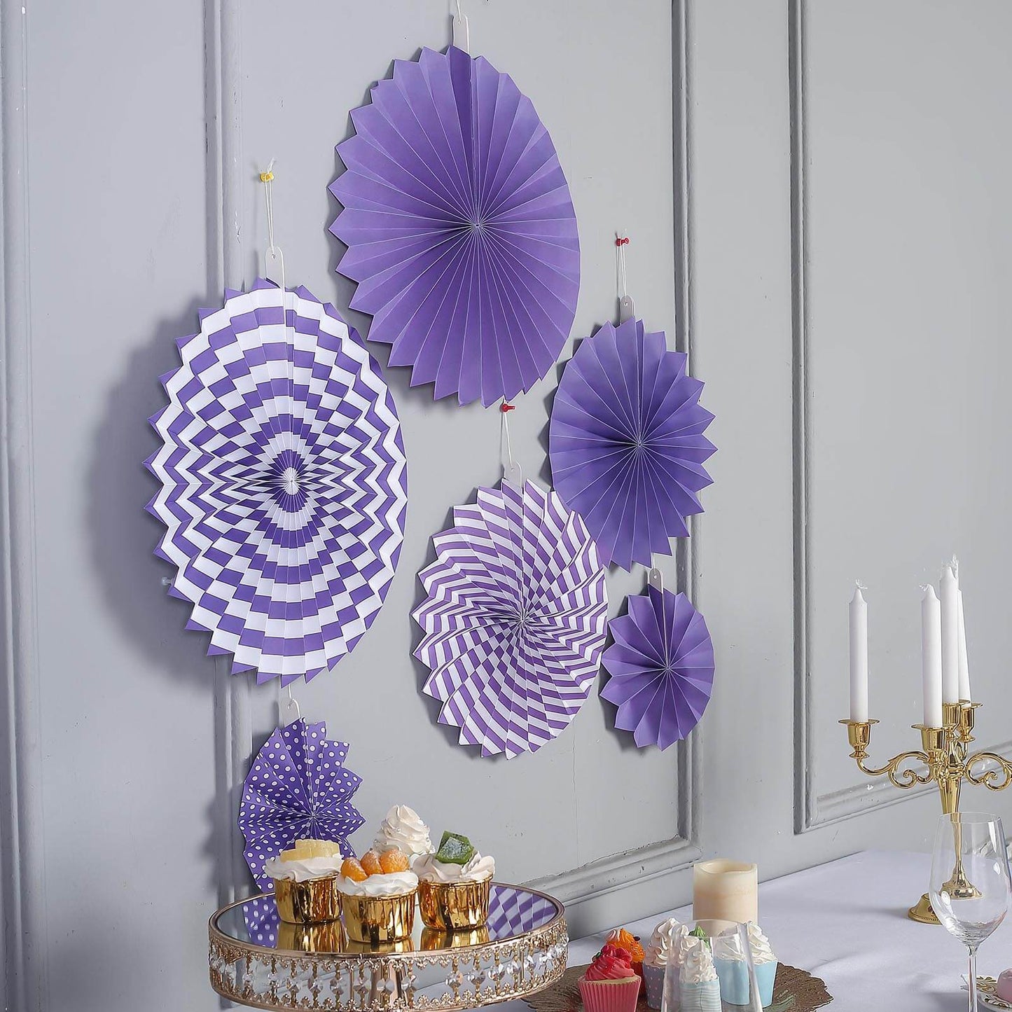 Purple hanging paper fan decorations set on a wall backdrop.