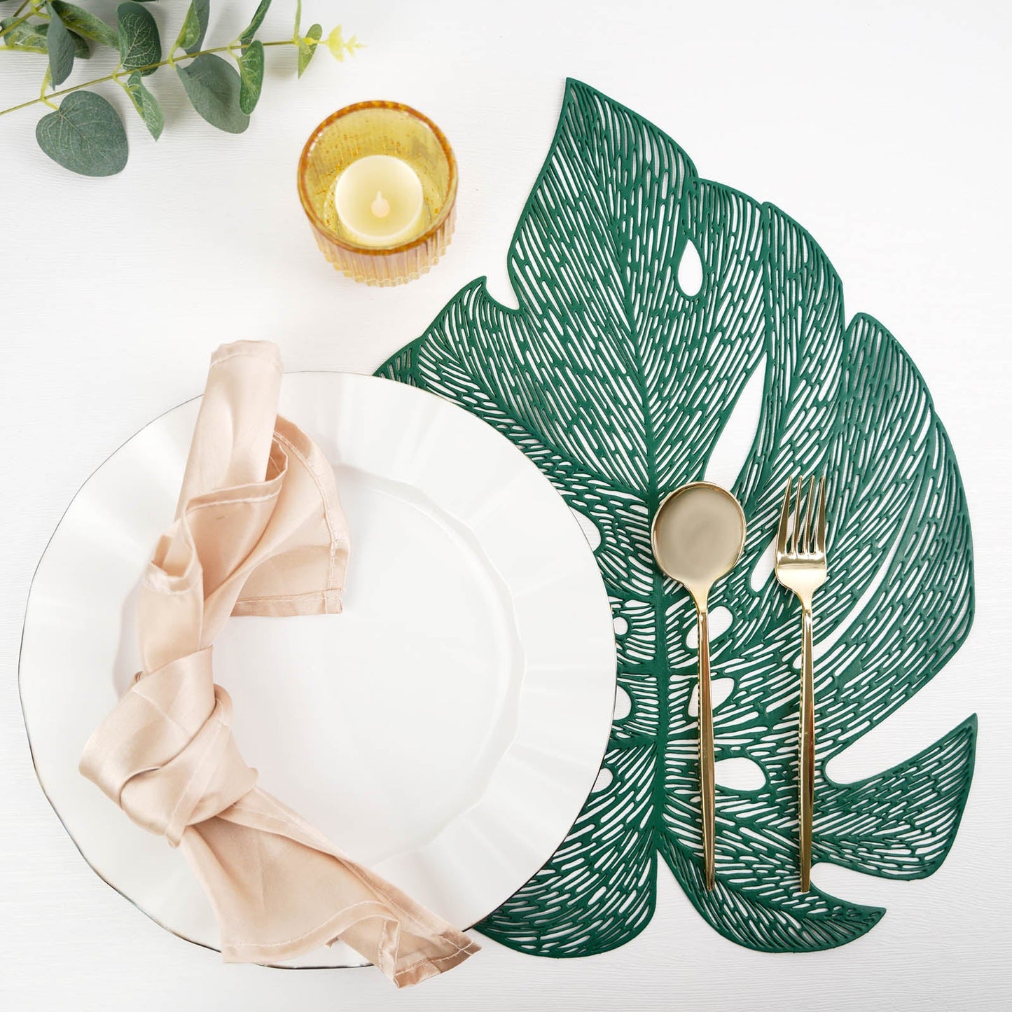 Green monstera leaf placemat with elegant table setting.