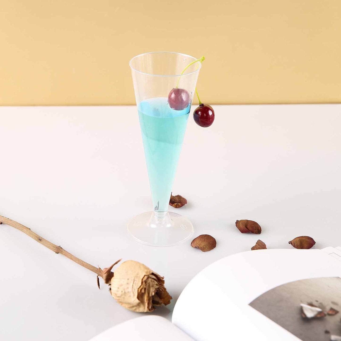Clear plastic trumpet champagne flute with blue drink and cherry garnish.