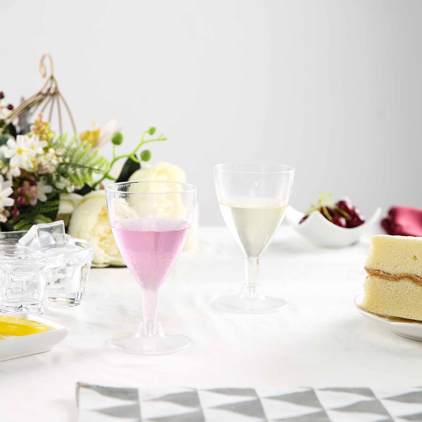 Clear plastic short hollow stem wine glasses on a table with pink and clear beverages.
