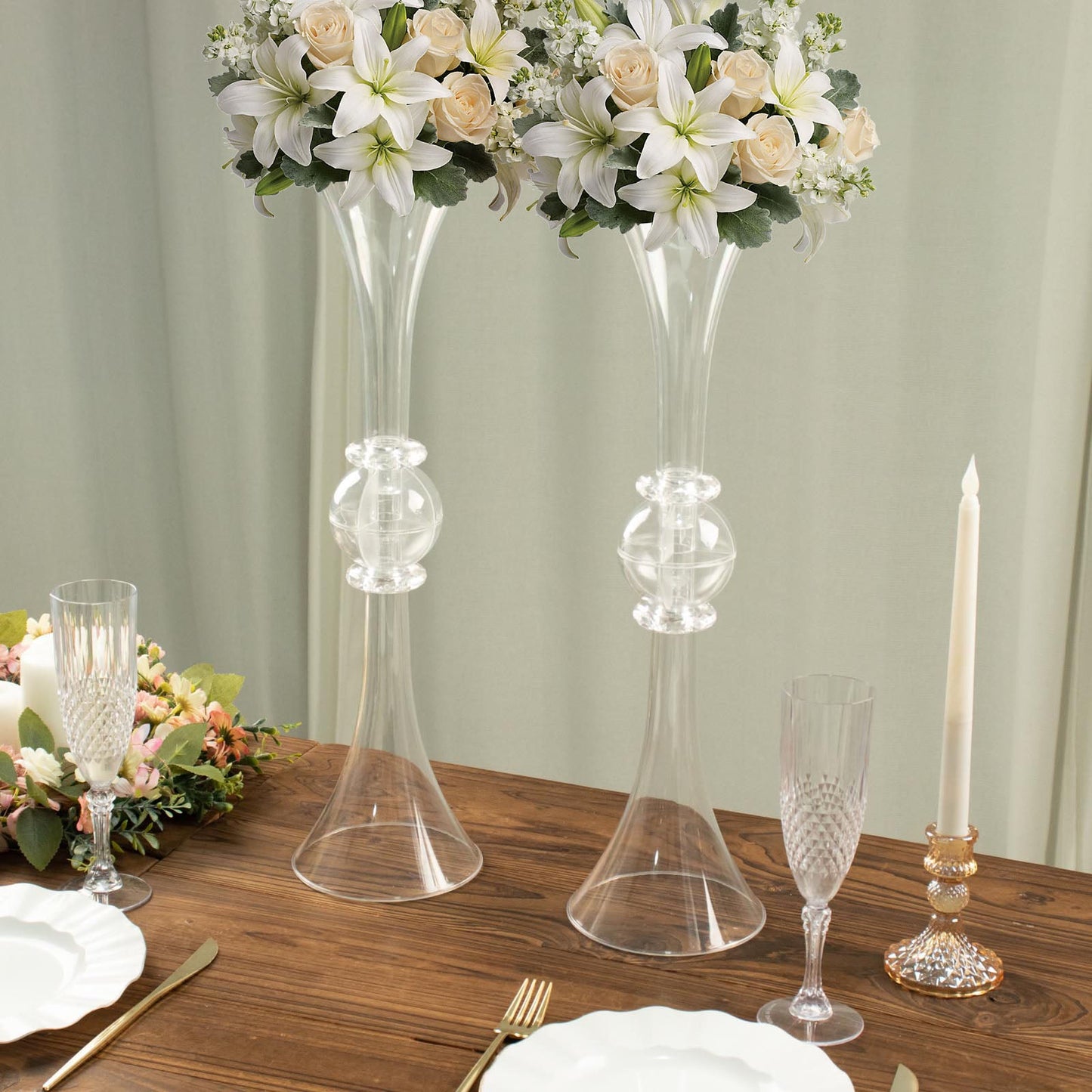Clear crystal trumpet vases with floral arrangements on a wooden table.