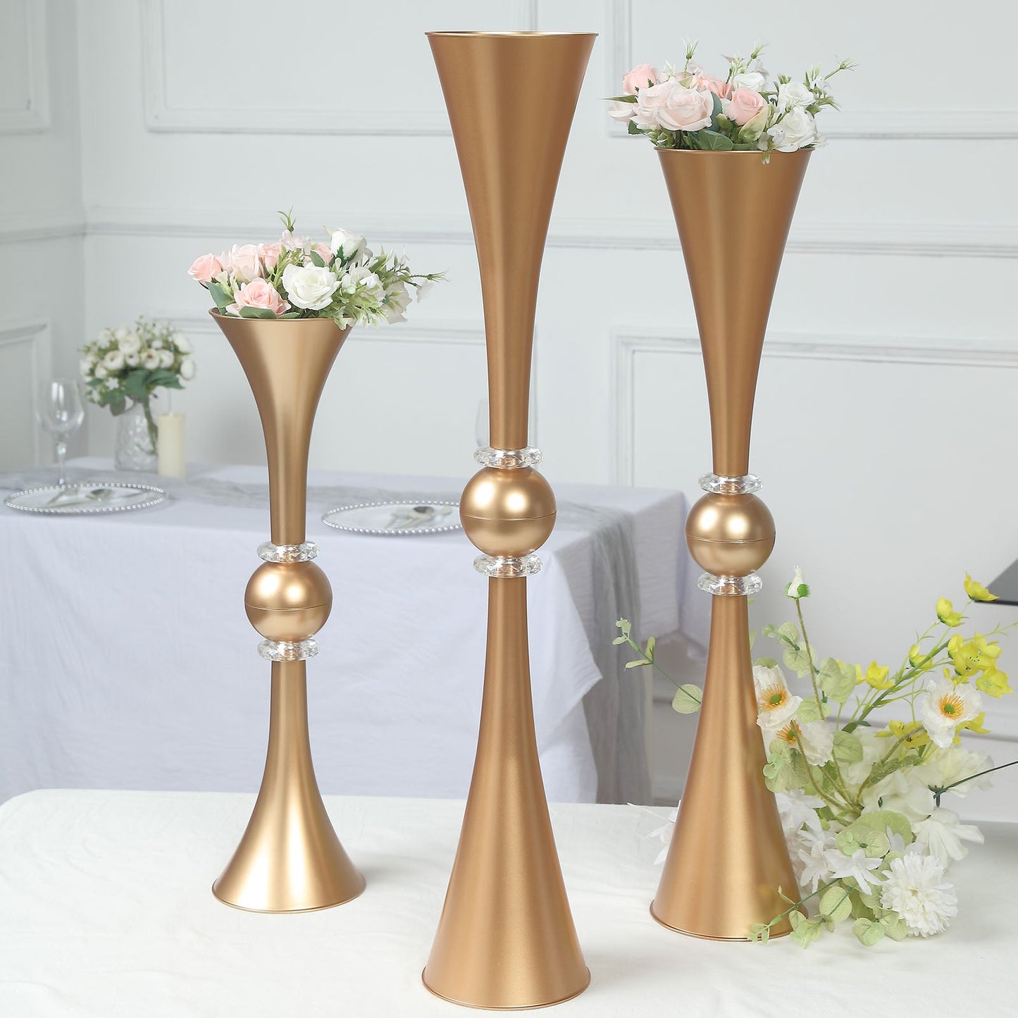 Gold crystal embellished trumpet vases with floral arrangements.