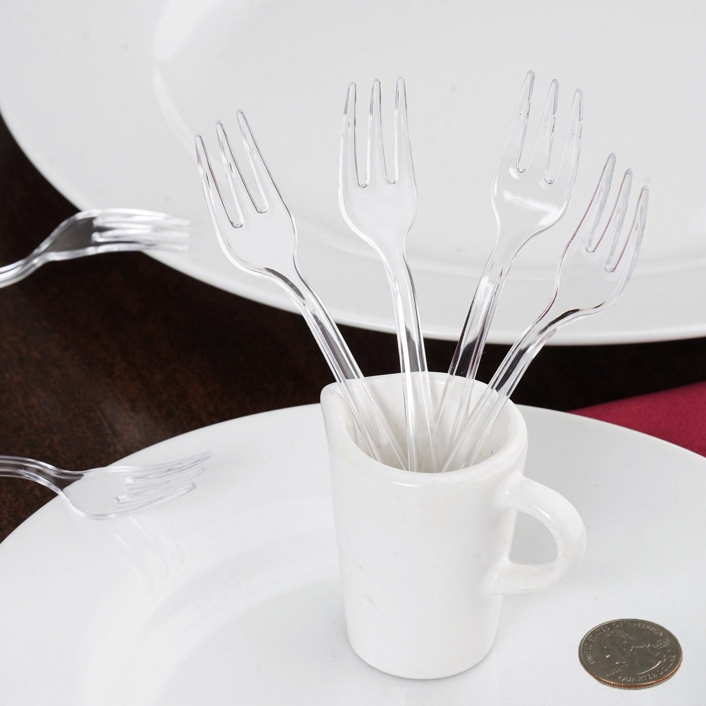 Clear mini heavy duty plastic forks in a cup on a white plate.