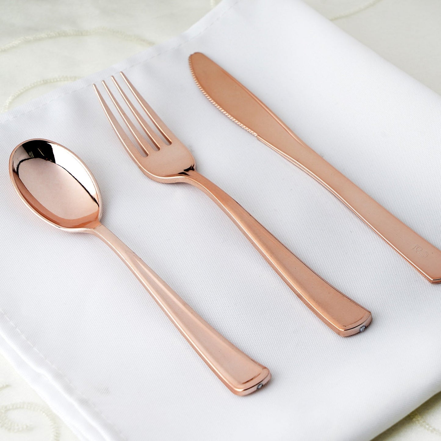 Metallic rose gold heavy duty plastic silverware set on a white napkin.