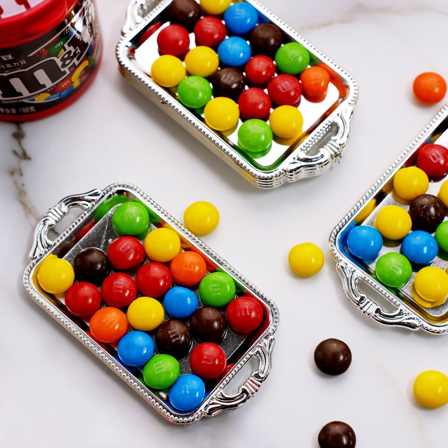 Silver rectangular mini party favor trays filled with colorful candy.