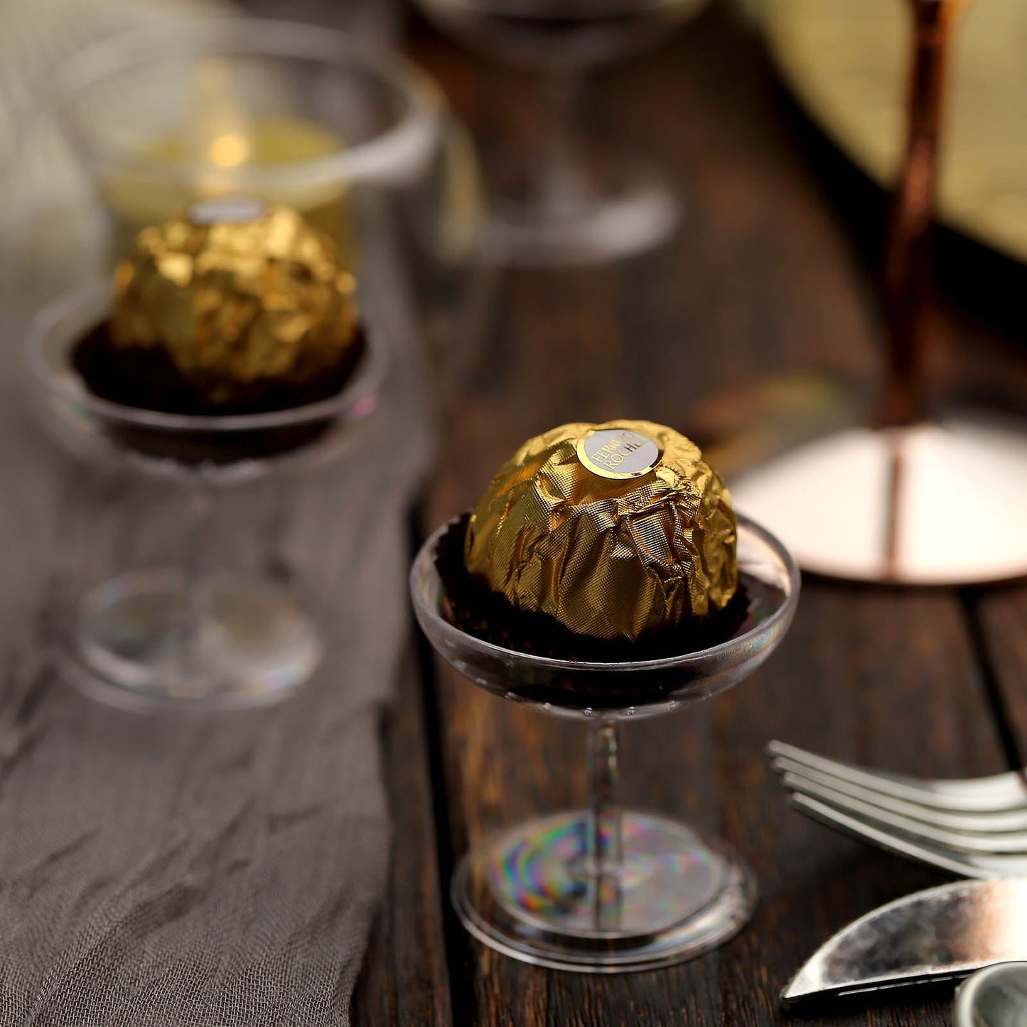 Clear dessert cups filled with treats on a wooden table.
