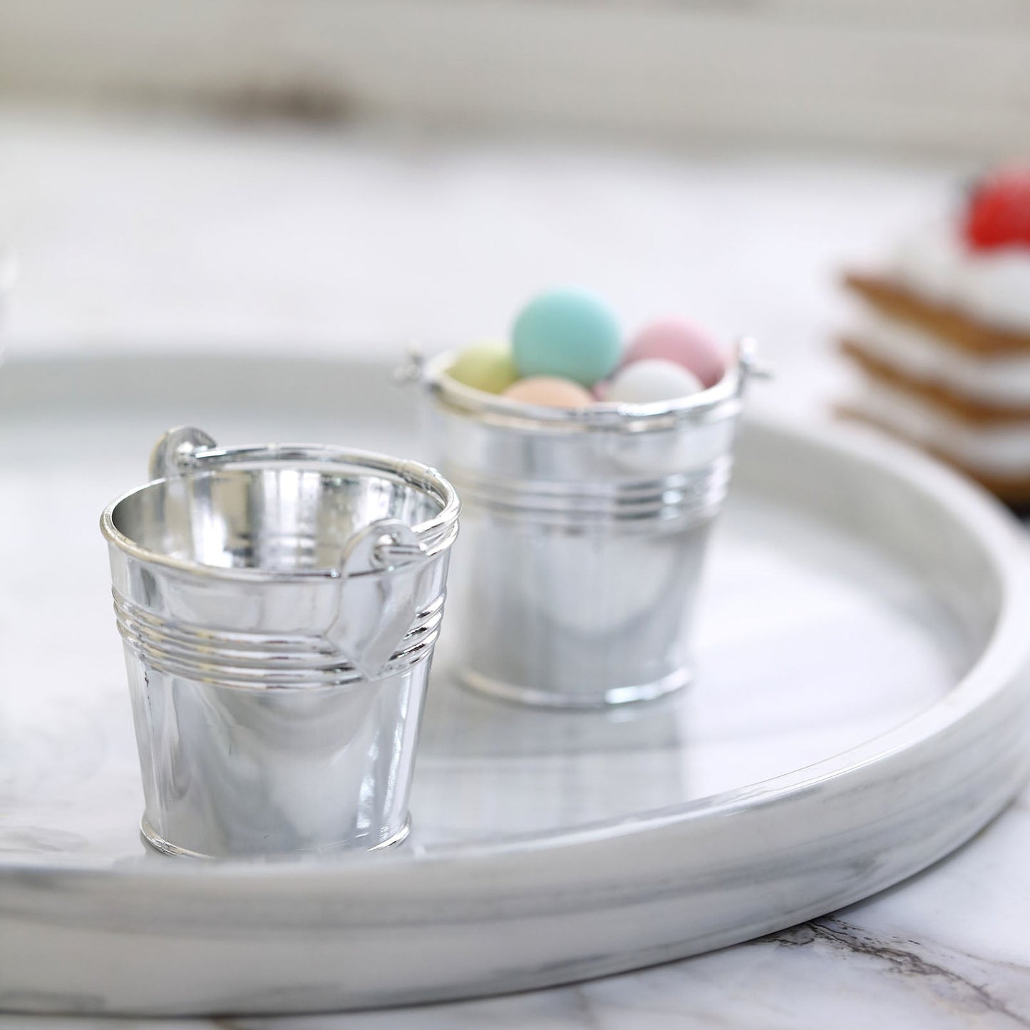 Silver mini pail buckets filled with pastel candy on a marble tray.