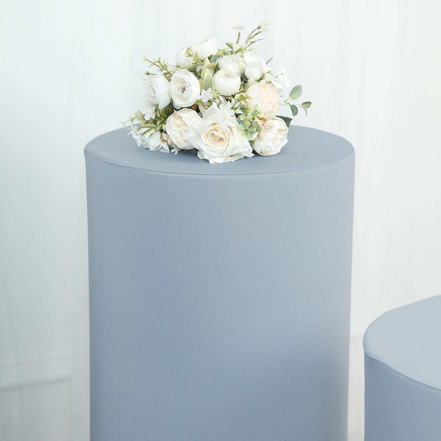Dusty blue spandex pedestal stand cover with floral arrangement on top.