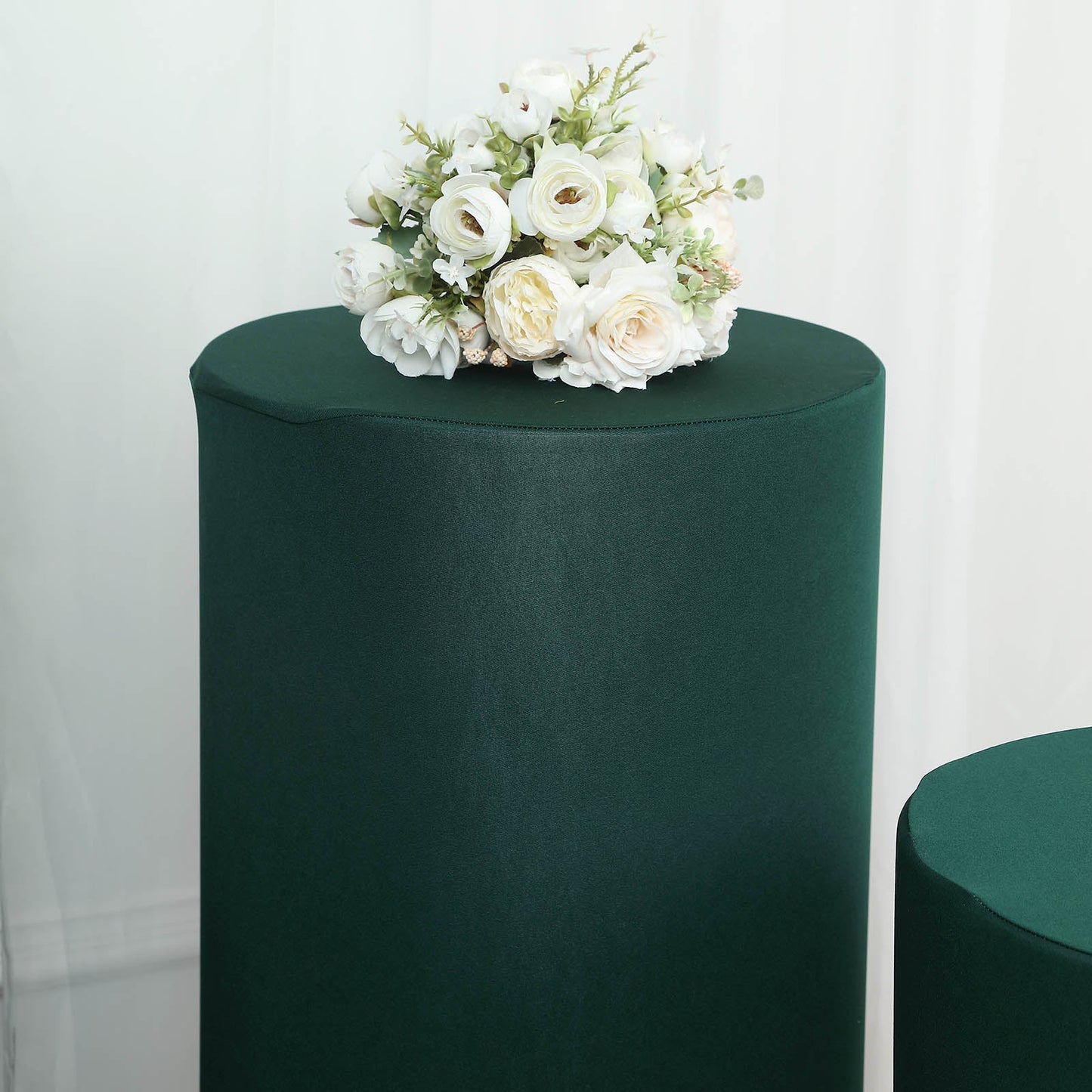 Emerald green spandex pedestal stand covers with a floral arrangement on top.